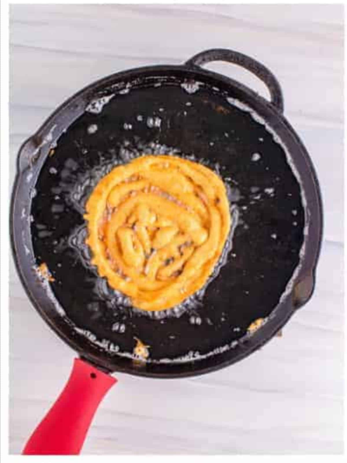 Drizzling funnel cake recipe batter into hot oil in a cast iron skillet.