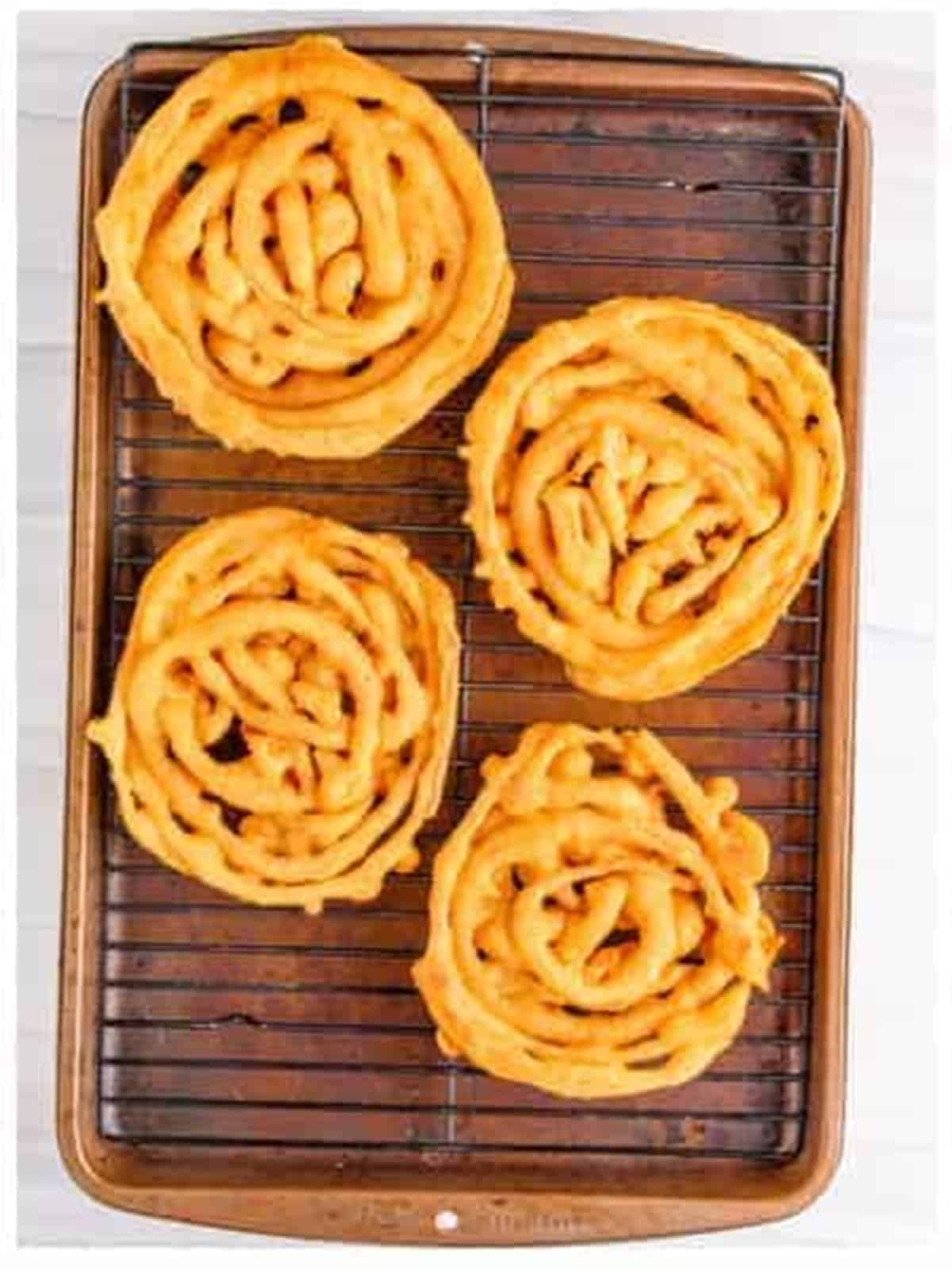 Golden fried funnel cakes draining on a wire rack.