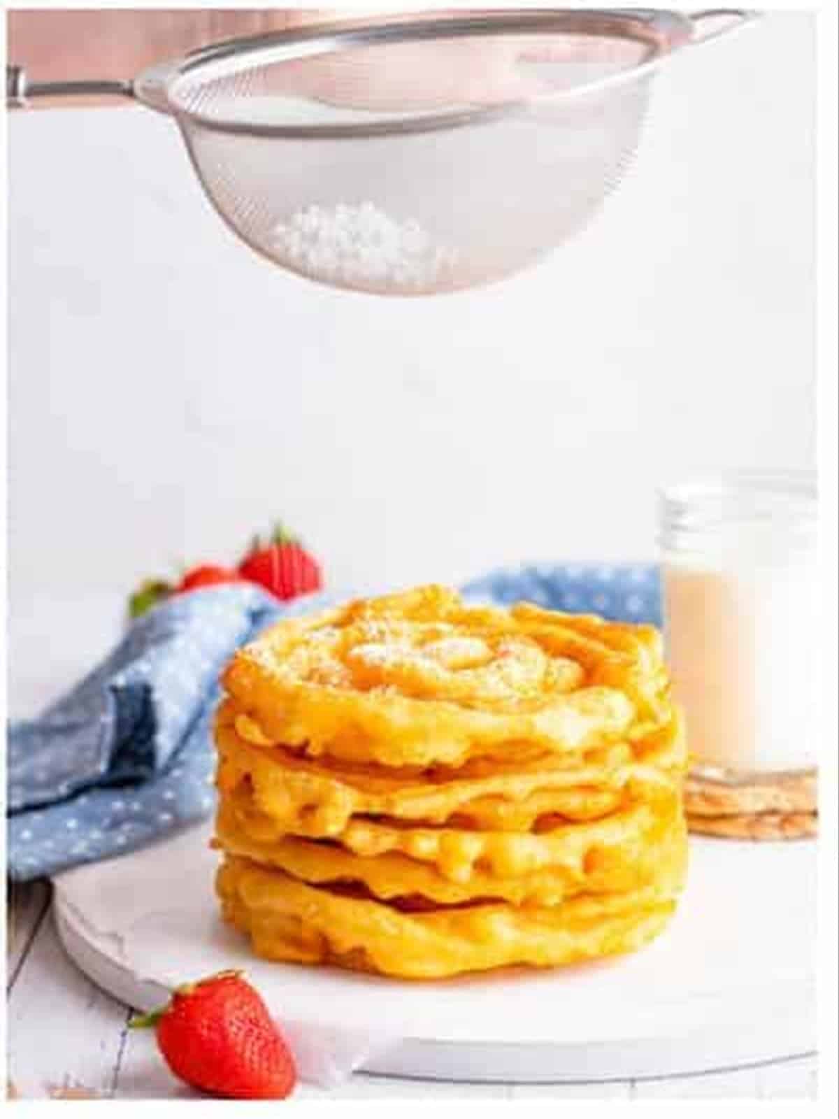 Dusting powdered sugar over a stack of funnel cakes.