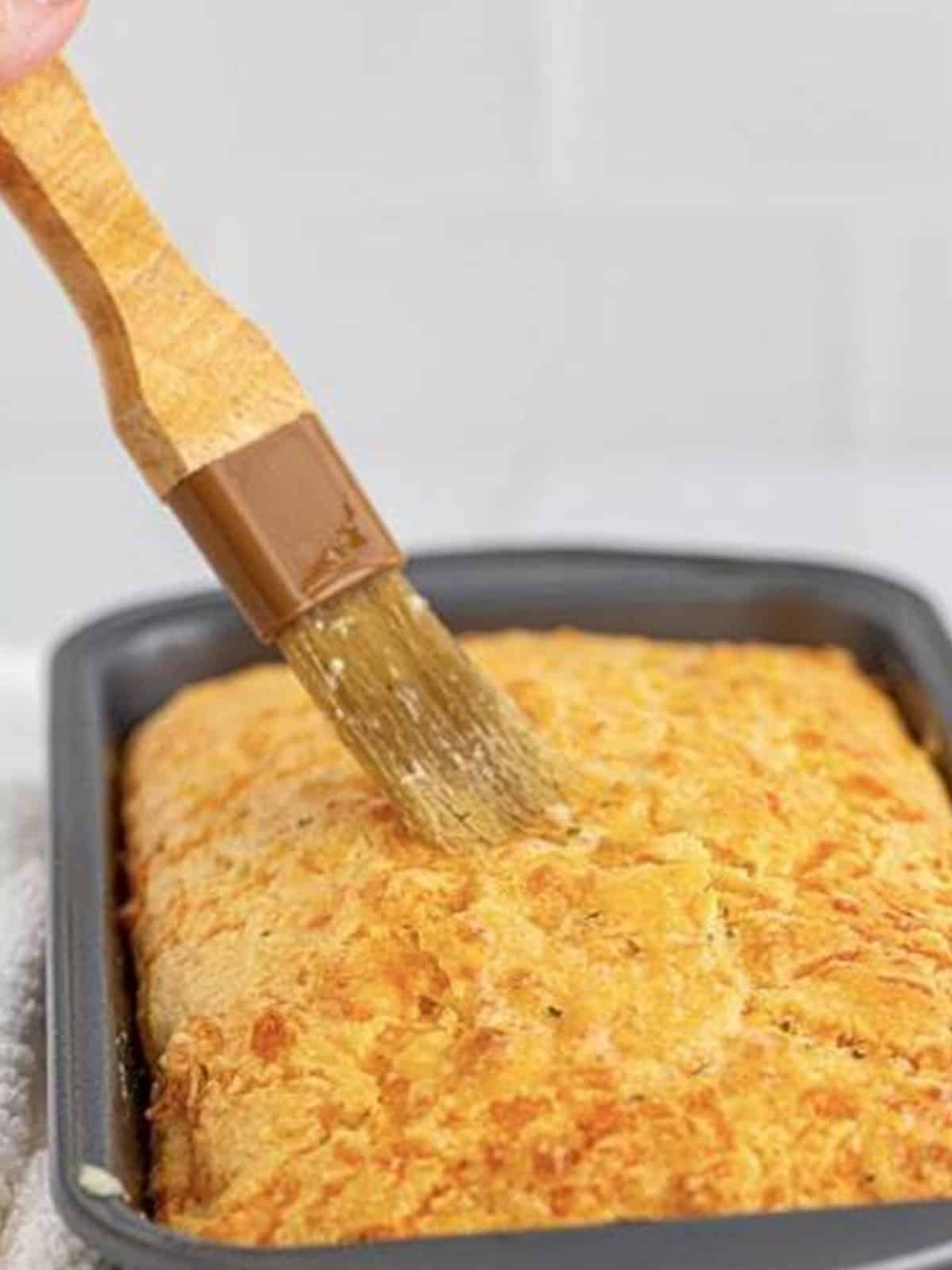 Garlic butter topping being brushed over the warm baked cheese bread.