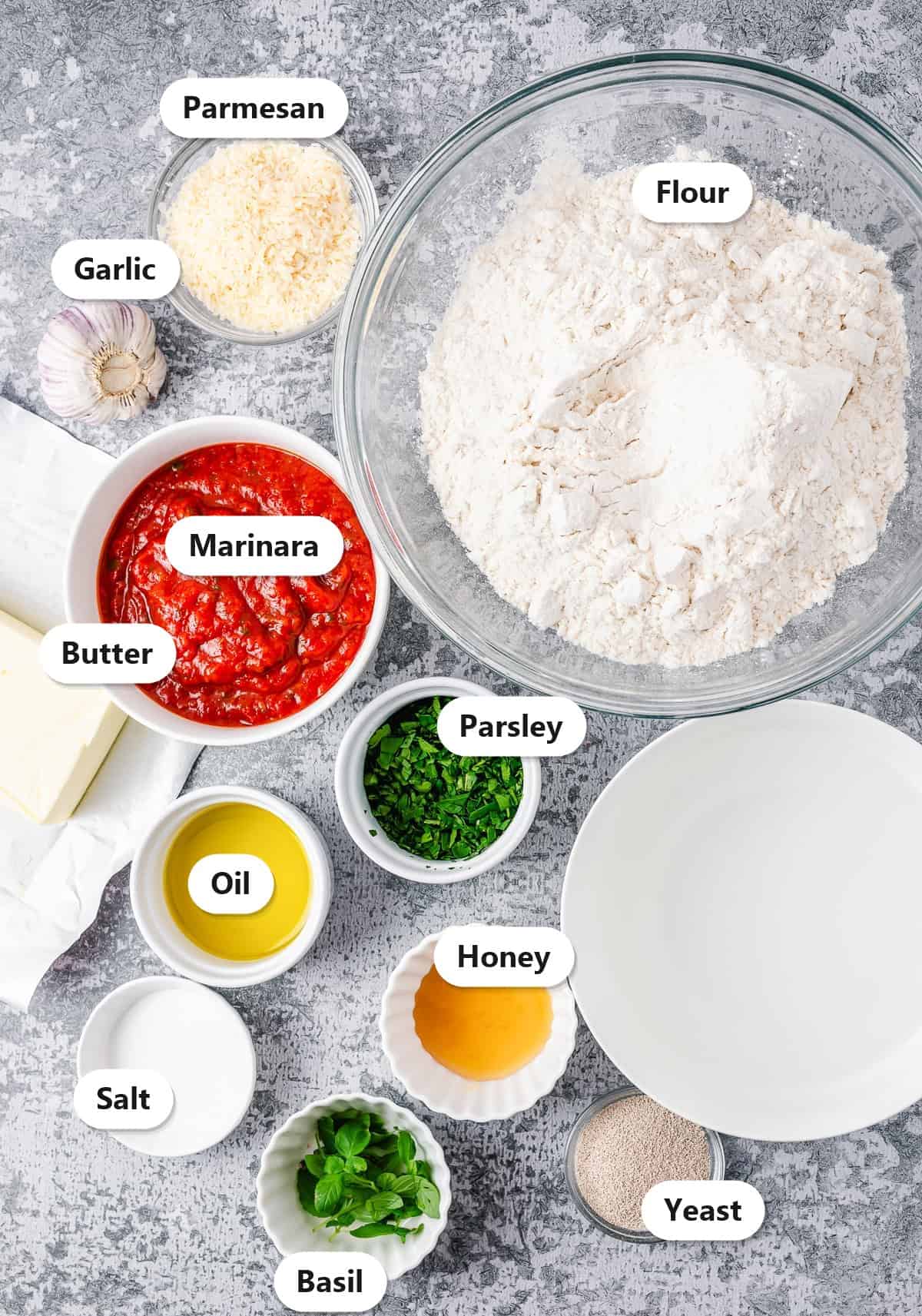Labeled ingredients for garlic knots including flour, marinara, butter, oil, garlic, parmesan, parsley, basil, honey, salt, and yeast.