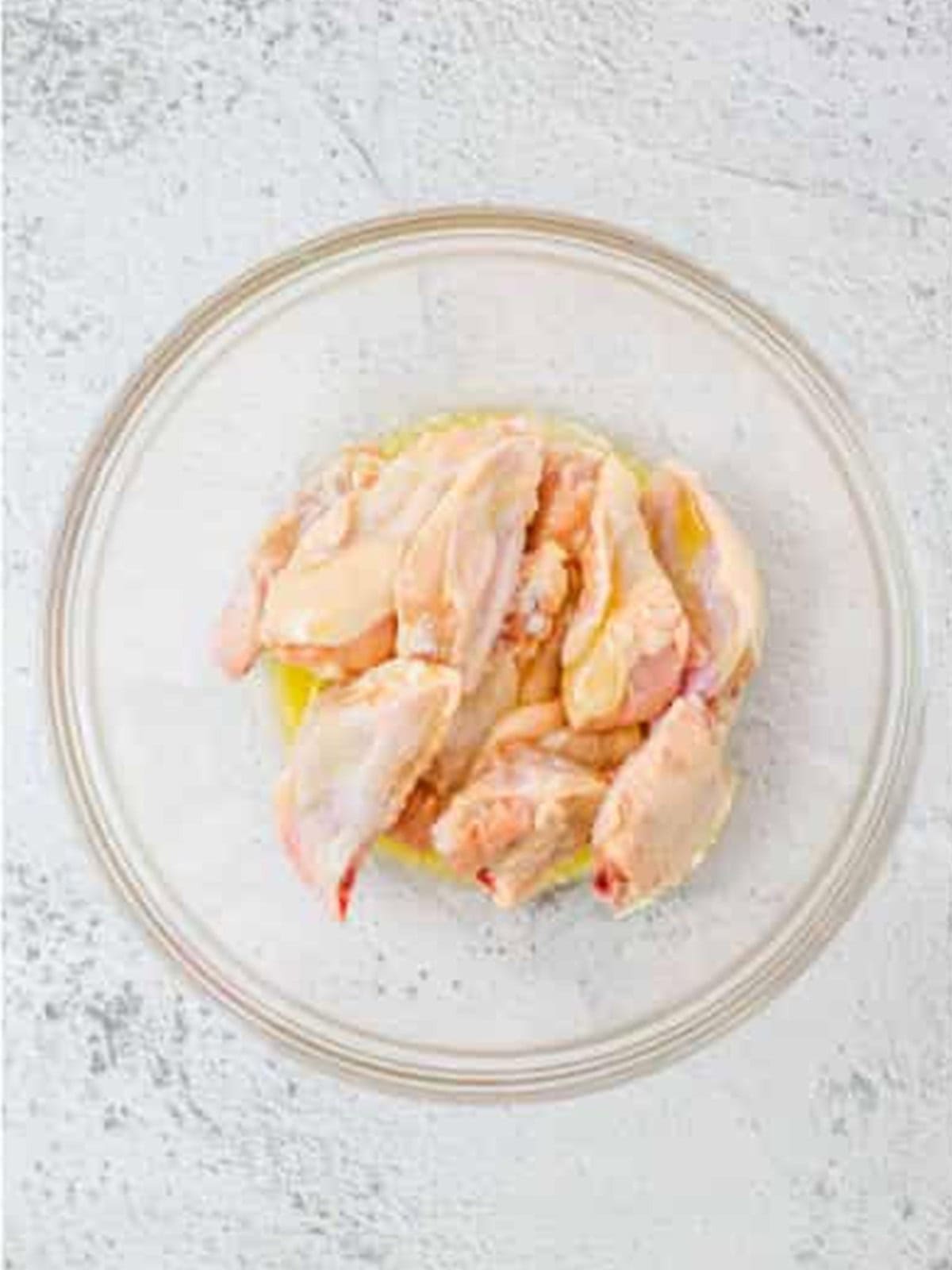 Raw chicken wings tossed in melted butter in a glass bowl for garlic parmesan wings.