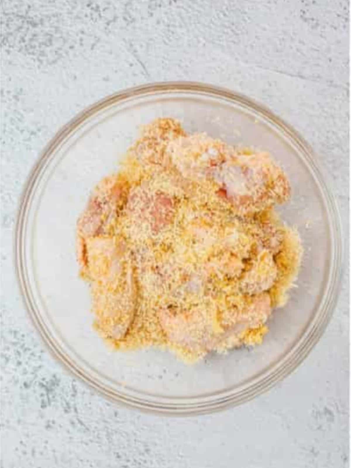 Chicken wings coated in the parmesan and spice mixture in a glass bowl.