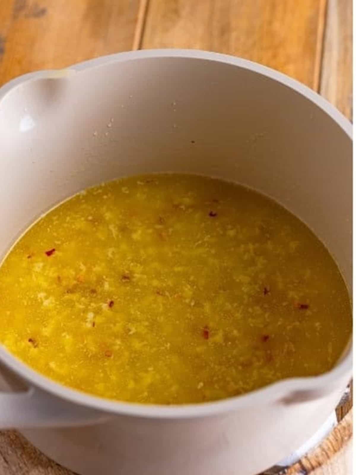 Melted garlic butter sauce with red pepper flakes in a bowl for Garlic Parmesan Wings.