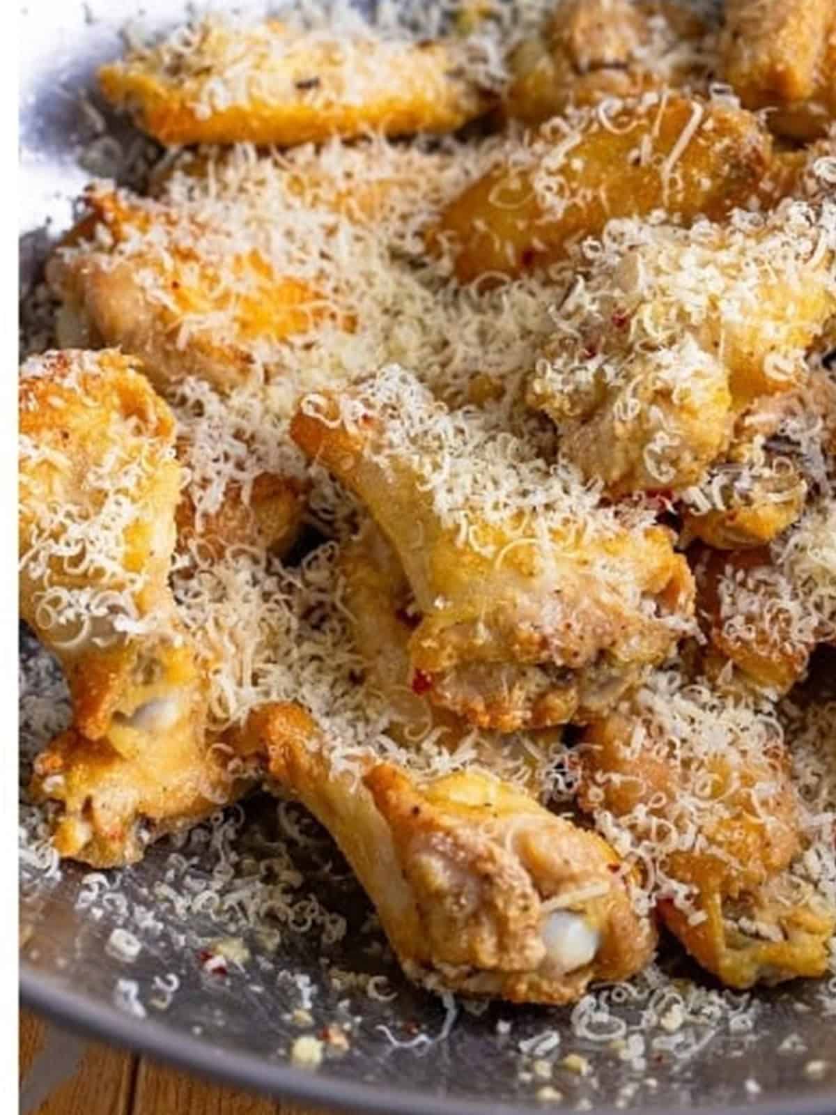 Sprinkling grated parmesan over the saucy Garlic Parmesan Wings.
