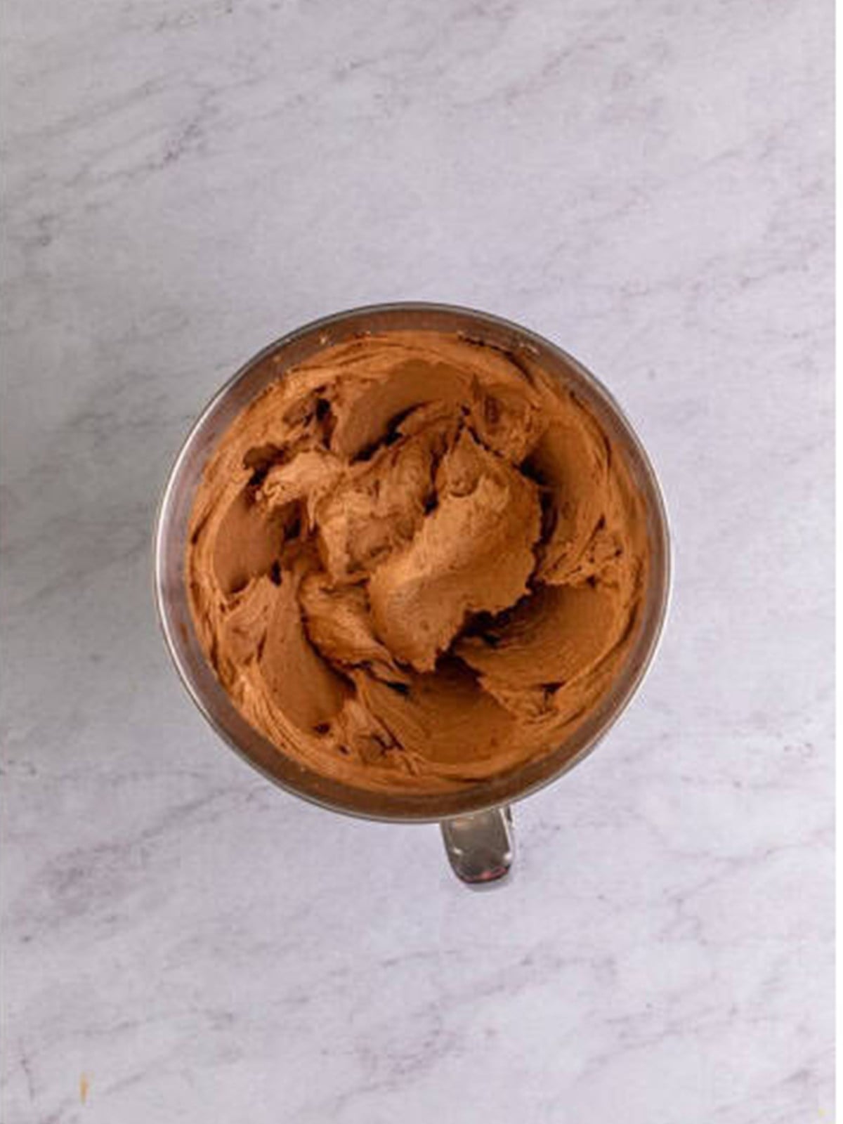 Whipped chocolate buttercream frosting in a stand mixer bowl.