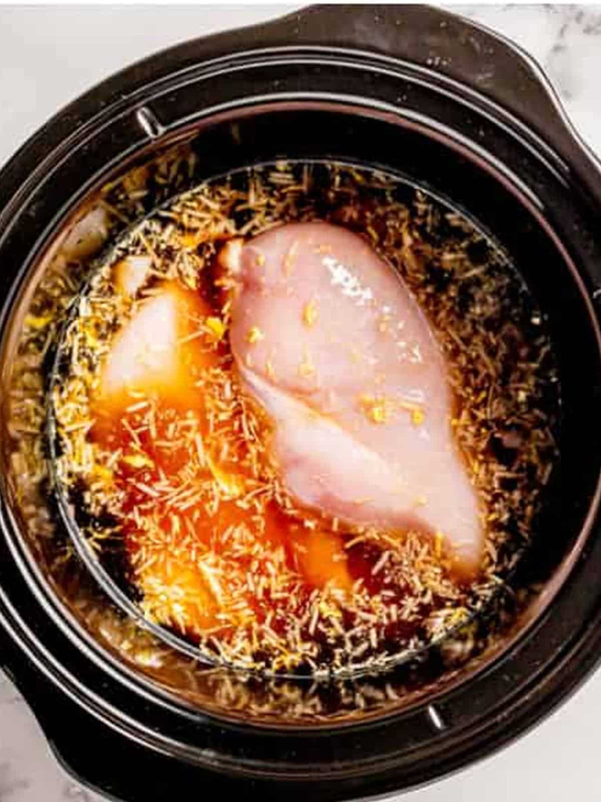 Raw chicken breasts in a slow cooker covered with ginger sauce.