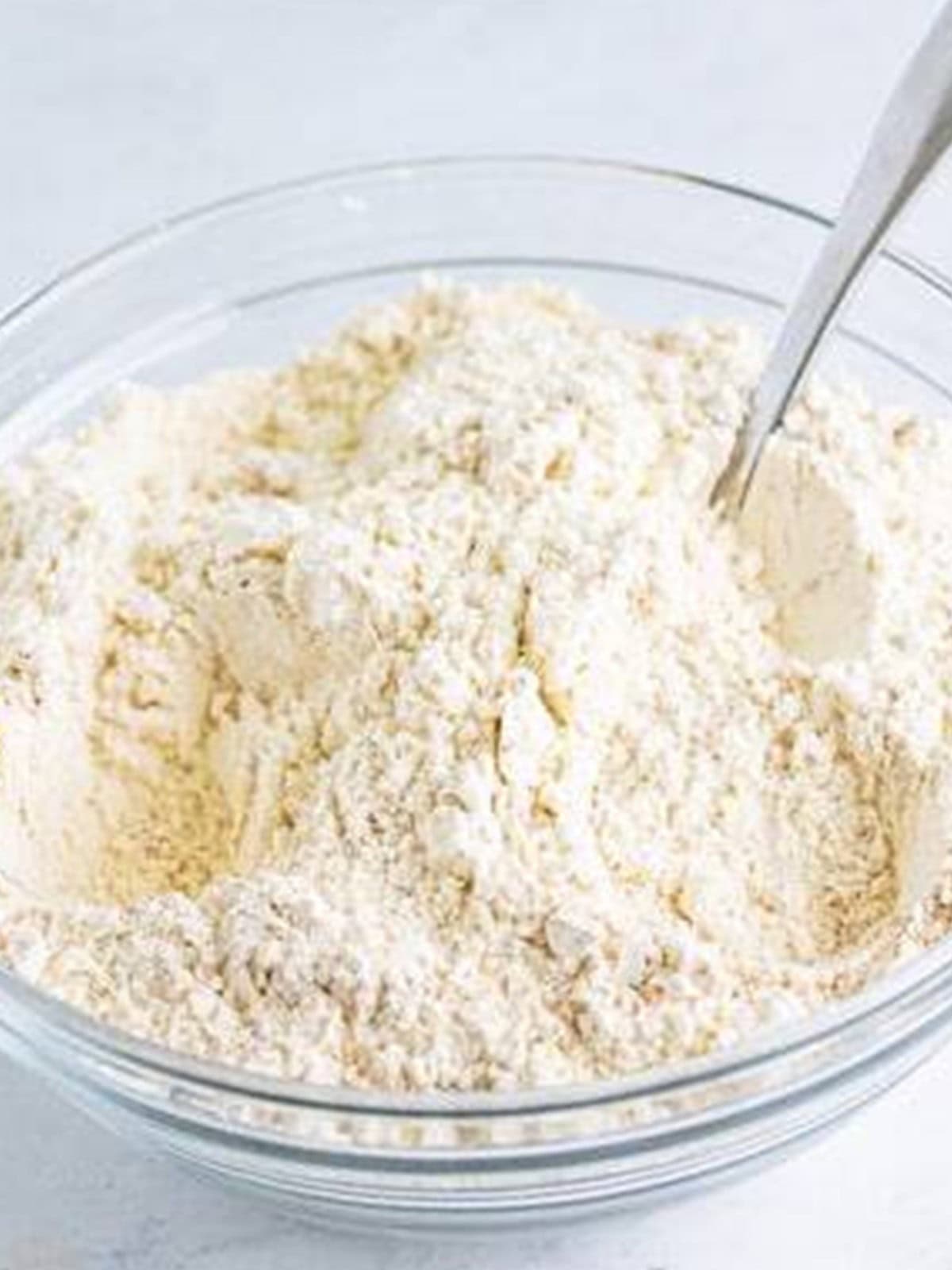 Flour, baking soda, and warm spices whisked together in a glass bowl.