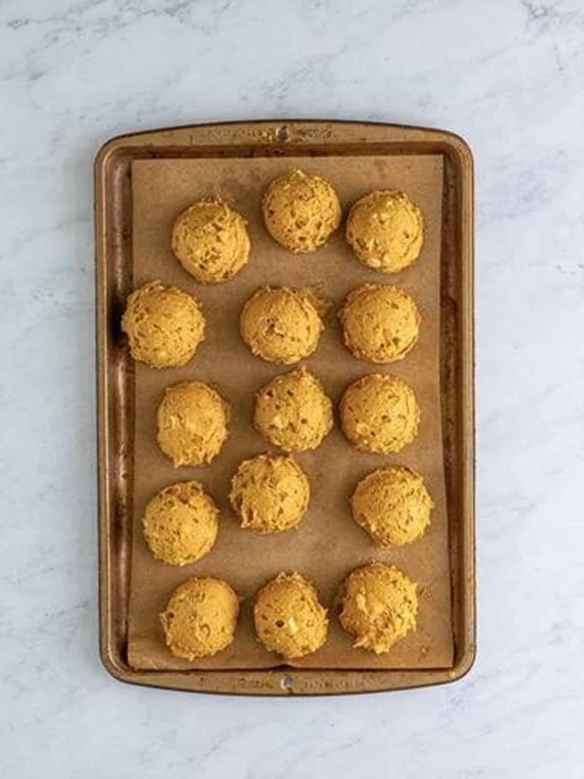 Scooped gingerbread cookie dough balls on a parchment lined sheet tray.