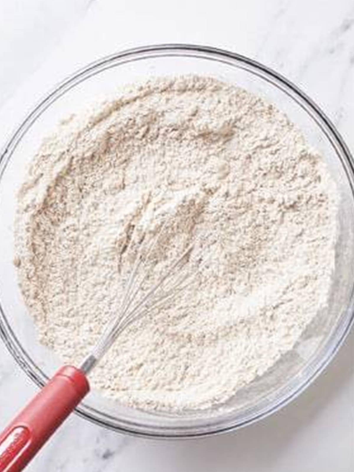 Whisking together flour, baking soda, salt, and warm gingerbread spices in a glass bowl.