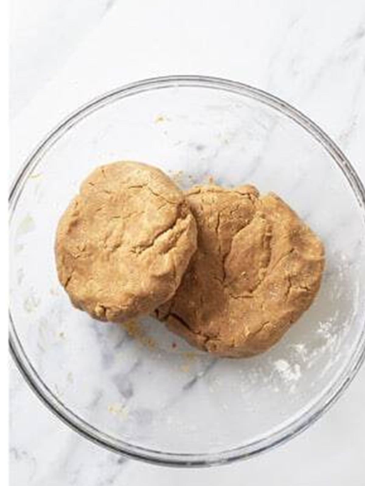 Gingerbread cookie dough formed into two disks in a glass bowl.