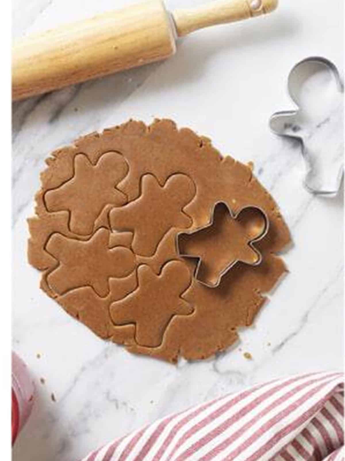 Cutting gingerbread men shapes from rolled out dough with a cookie cutter.