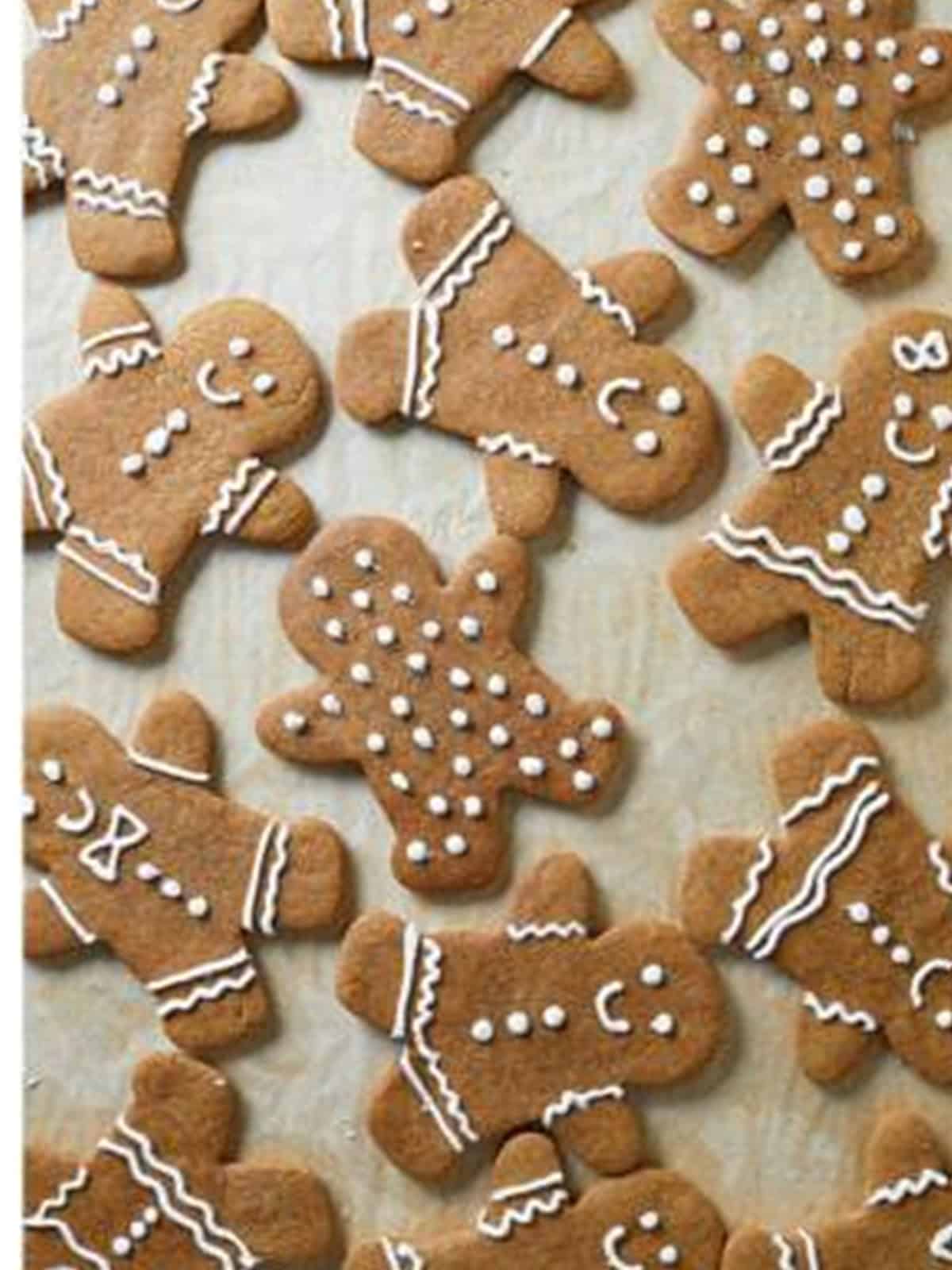 Baked gingerbread men decorated with white royal icing on parchment.