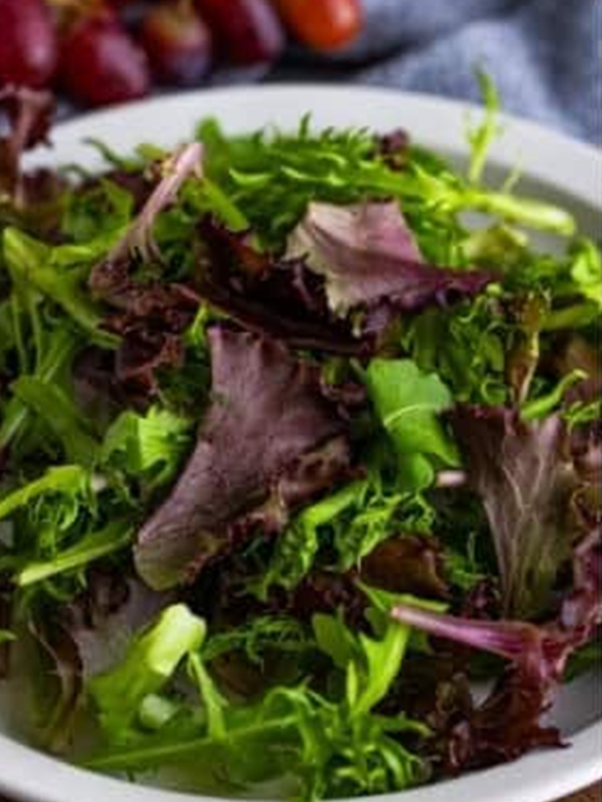 Fresh spring mix greens added to a white serving bowl for goat cheese salad.