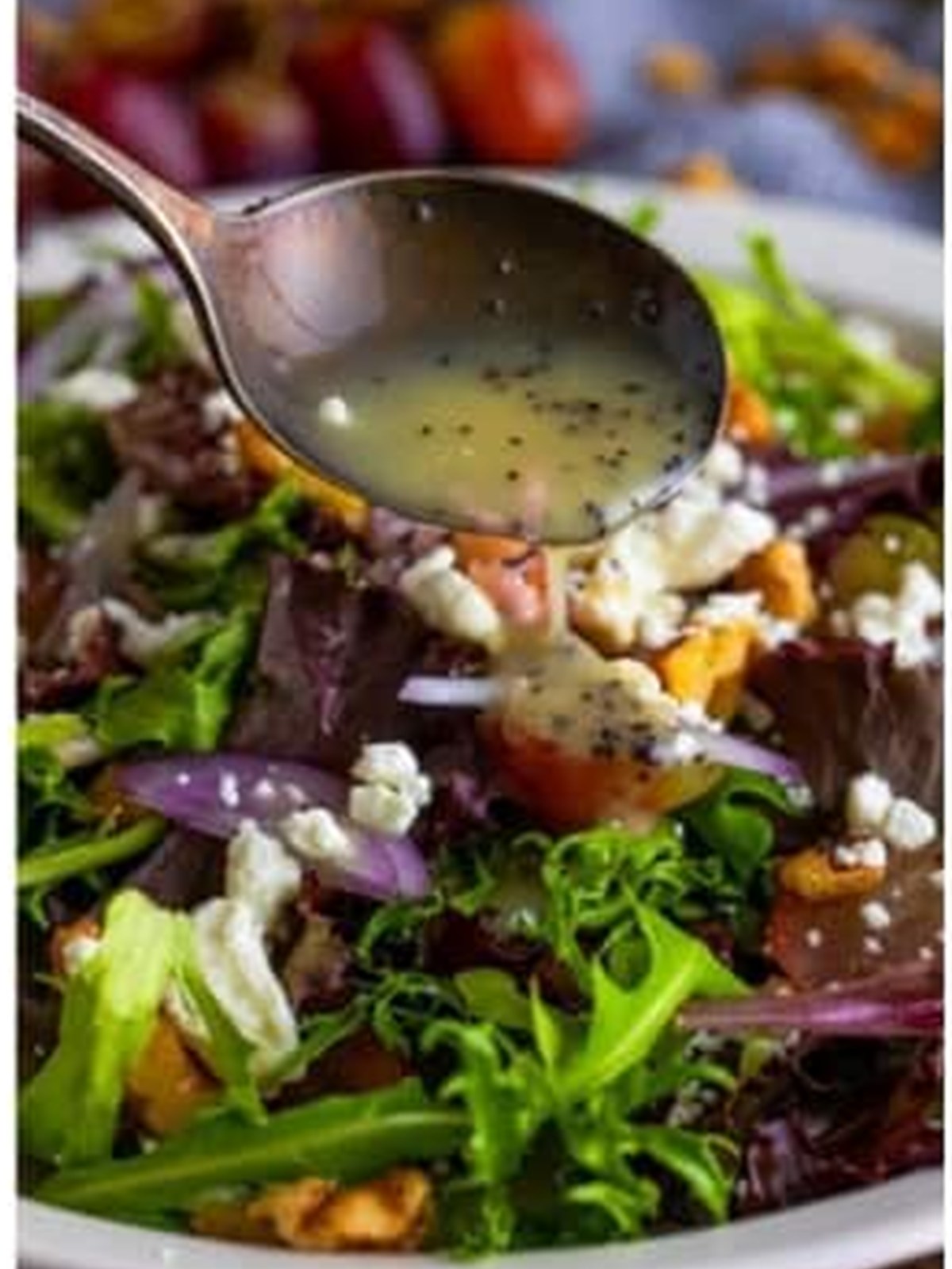 Pouring poppy seed dressing over the goat cheese salad with a spoon.
