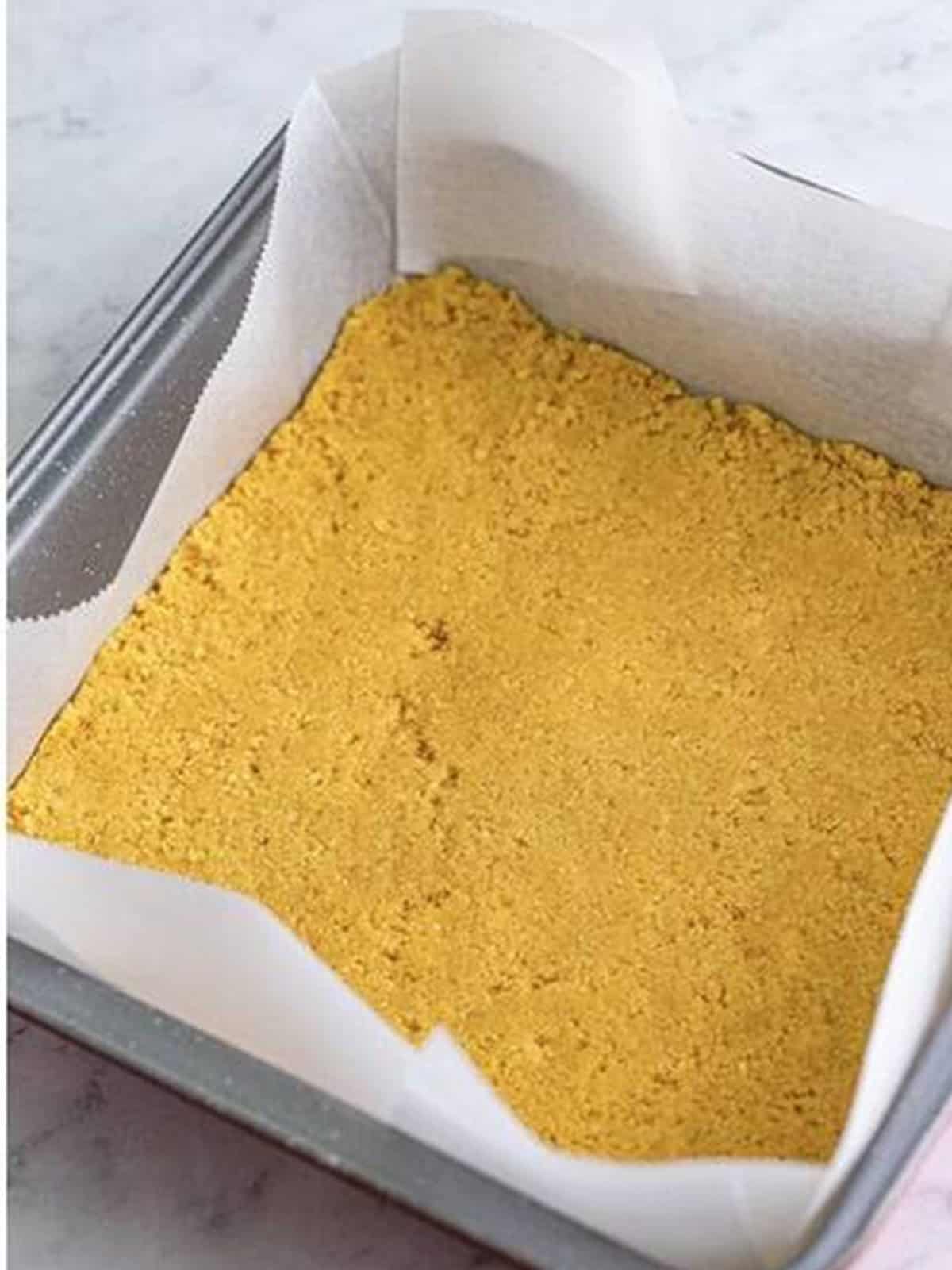 Golden Oreo crumb crust pressed into a parchment lined baking dish.