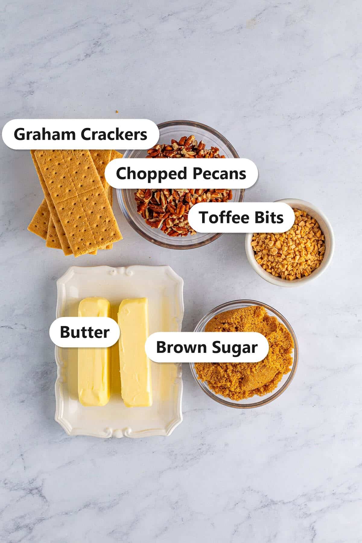 Labeled ingredients to make graham cracker toffee including graham crackers, chopped pecans, toffee bits, butter, and brown sugar.