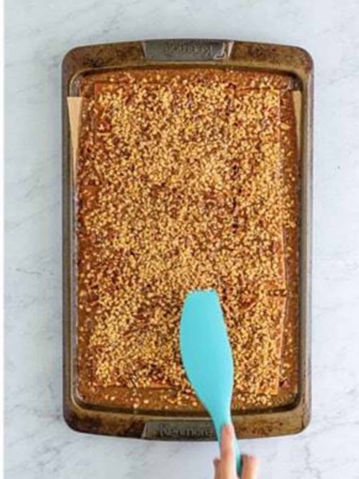 Pressing English toffee bits into the hot caramel with a spatula.