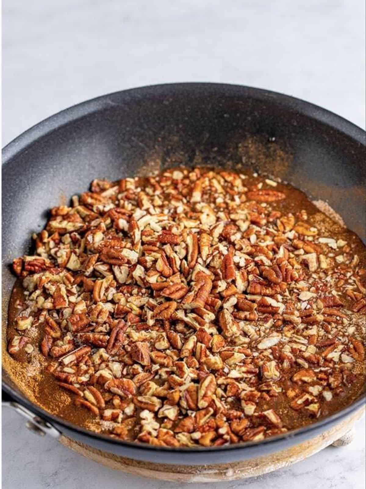 Pecans cooking in the skillet as the cinnamon sugar glaze thickens.
