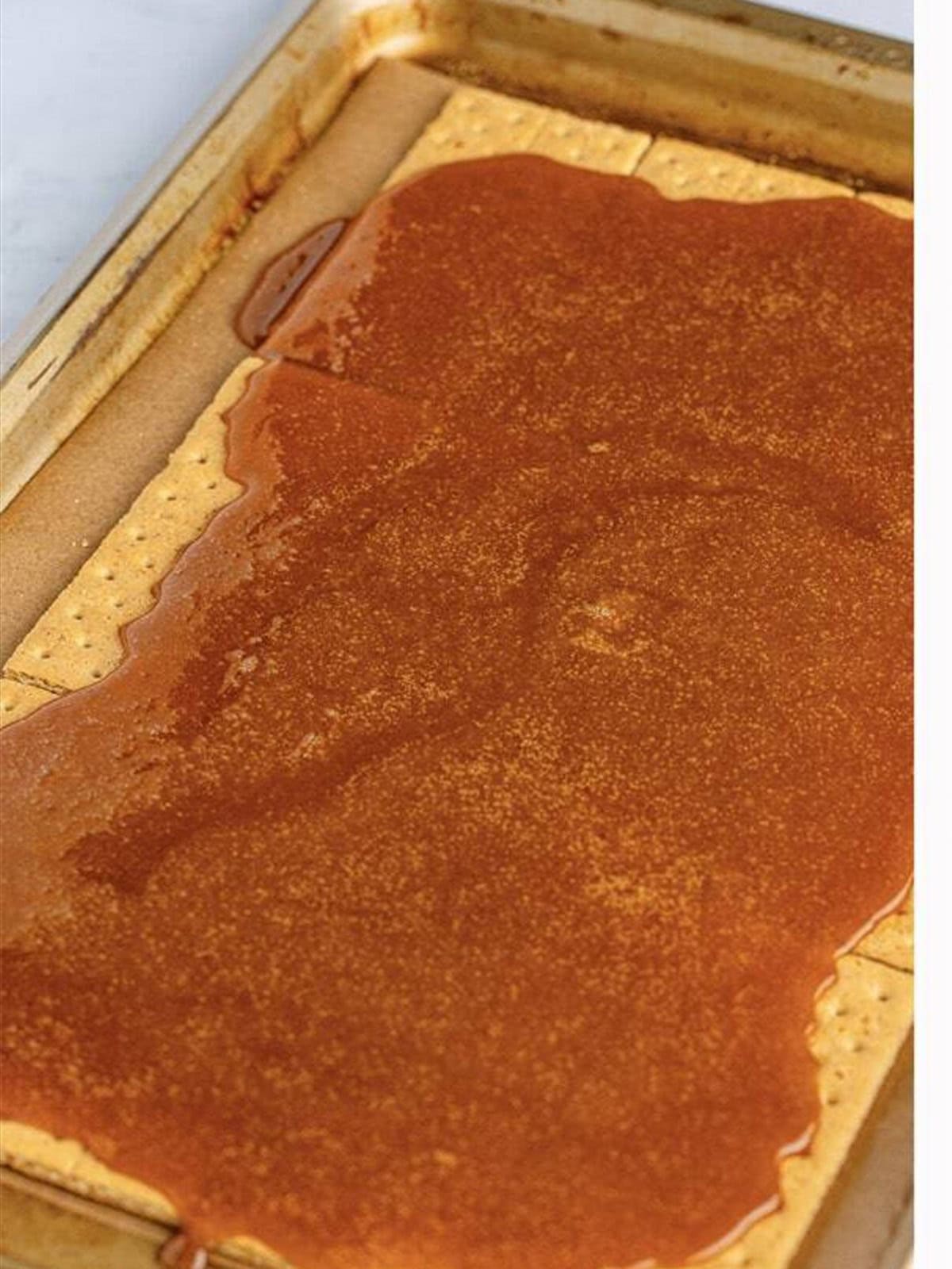 Graham crackers laid out in a single layer on a parchment-lined sheet tray.
