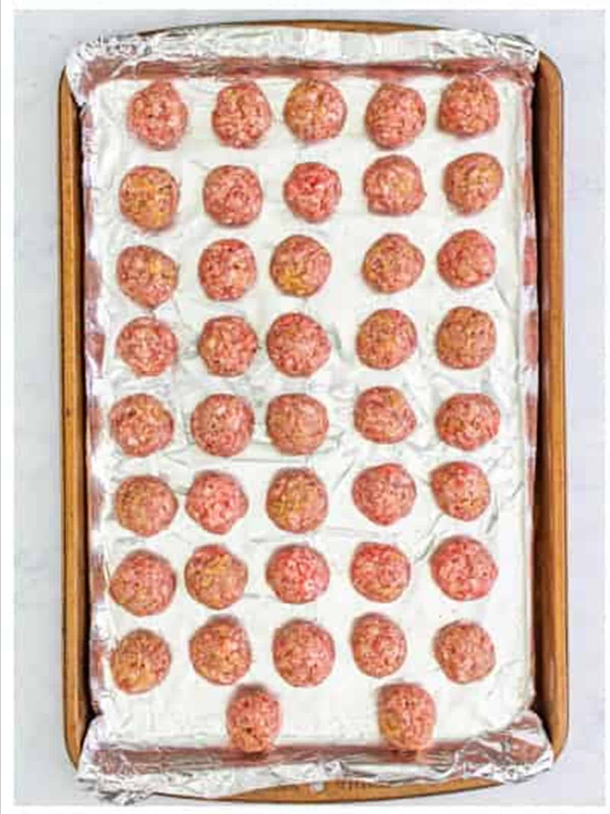 Rolled raw meatballs on a sheet tray for grape jelly meatballs.