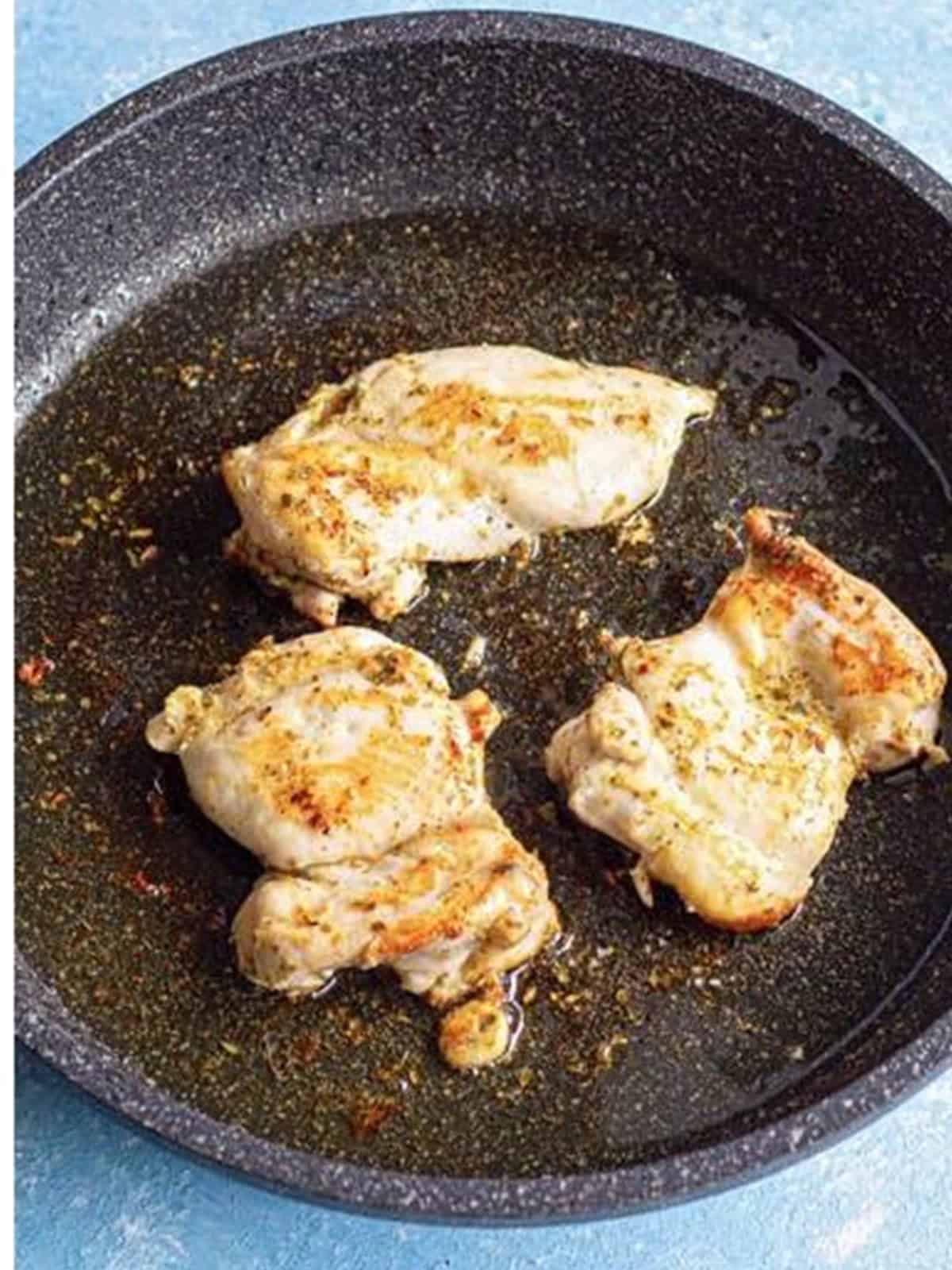 Marinated chicken thighs cooking in a skillet until golden.