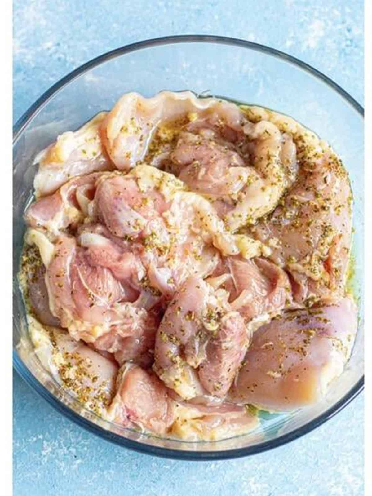 Chicken thighs tossed with Greek marinade in a bowl.