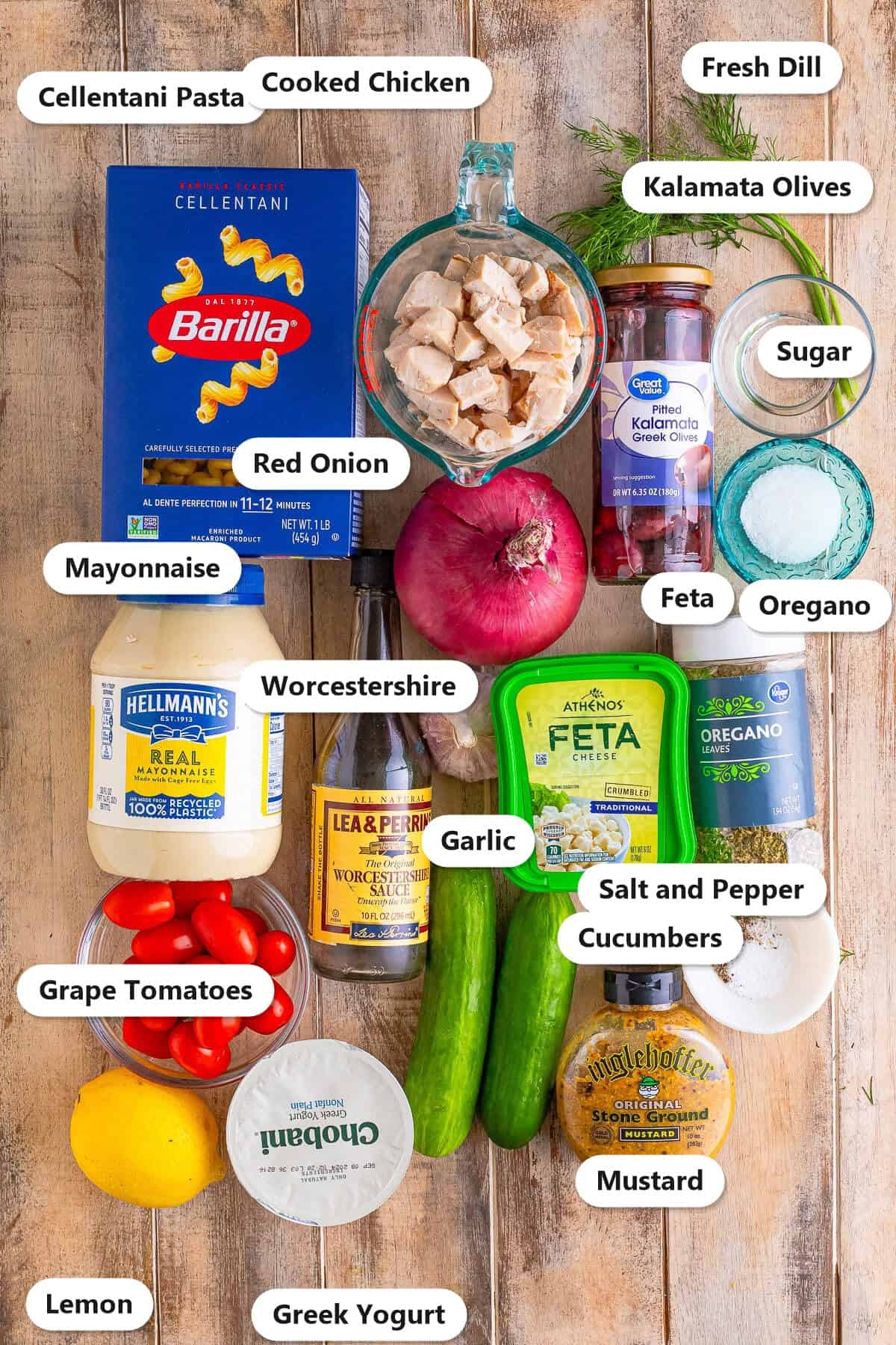 Ingredients to make Greek Pasta Salad laid out and labeled on a wooden counter.