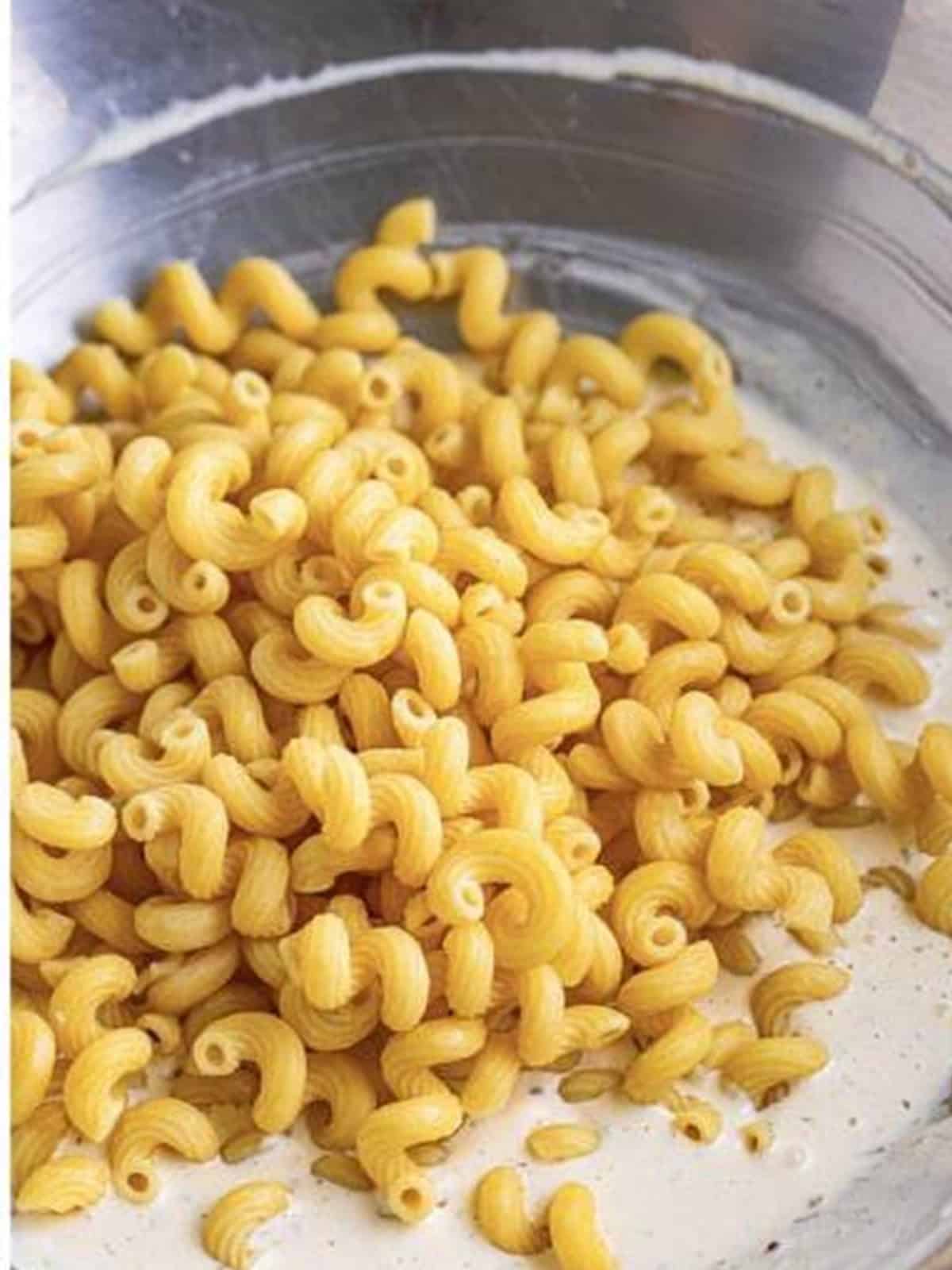 Cooked cellentani pasta added to the bowl of creamy dressing for Greek Pasta Salad.