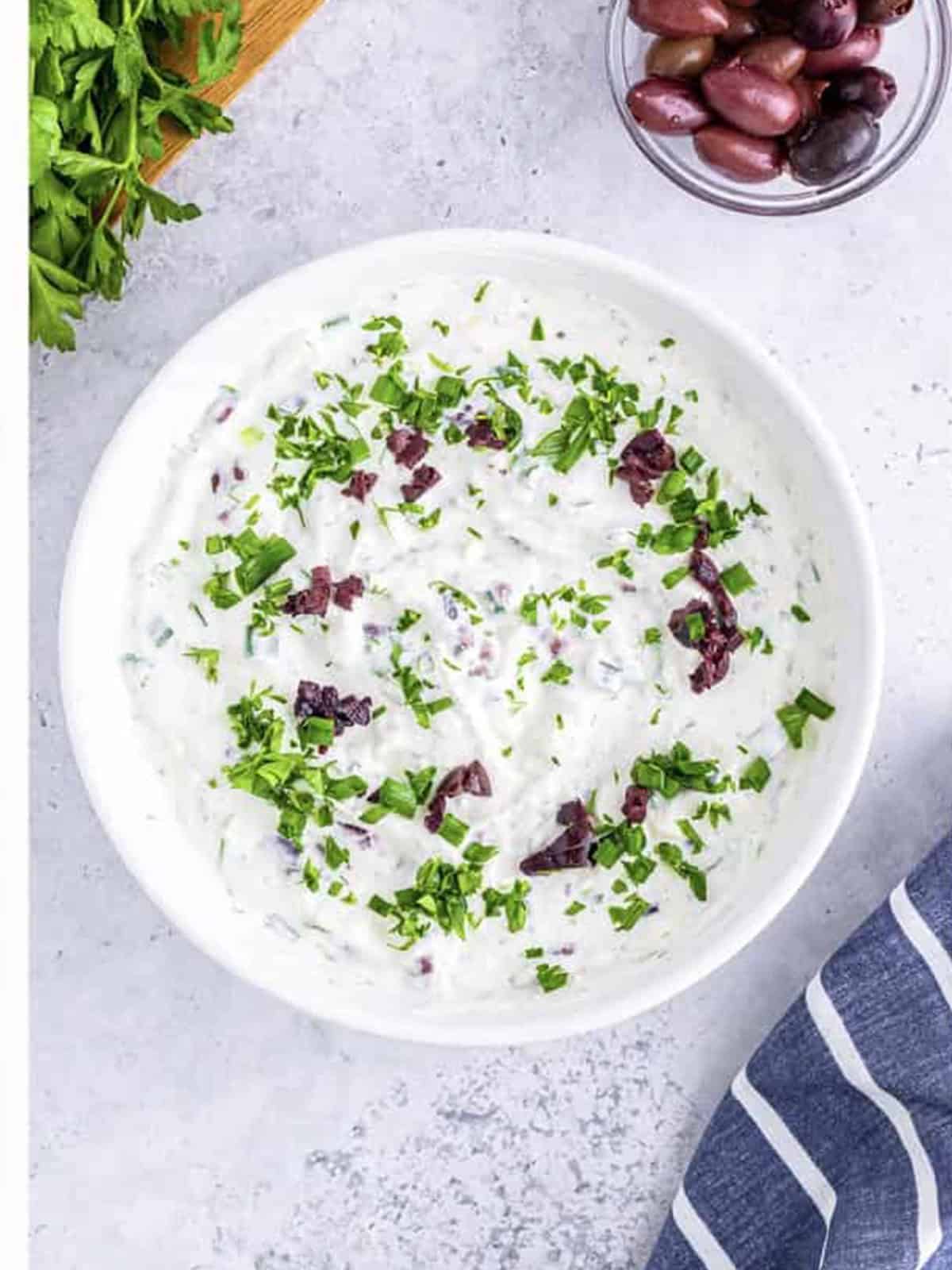 Finished greek yogurt dip in a bowl garnished with chopped herbs and olives.