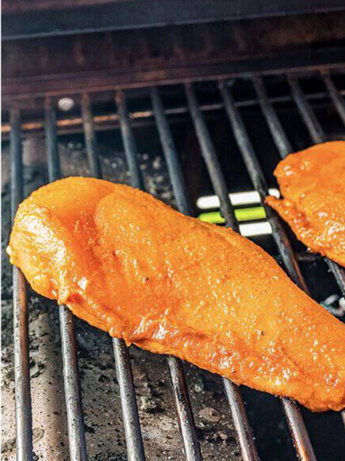 A marinated chicken breast cooking on a hot grill.