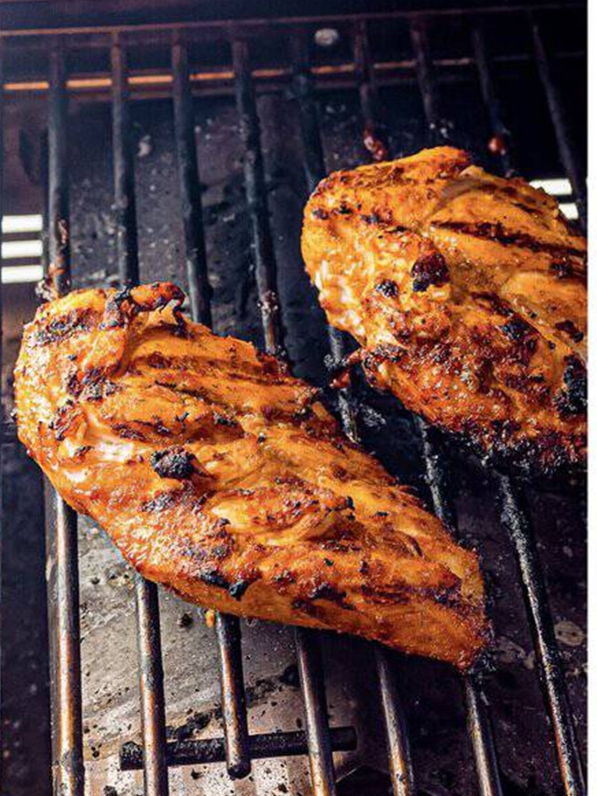 Grilled marinated chicken breasts with char marks on a grill.