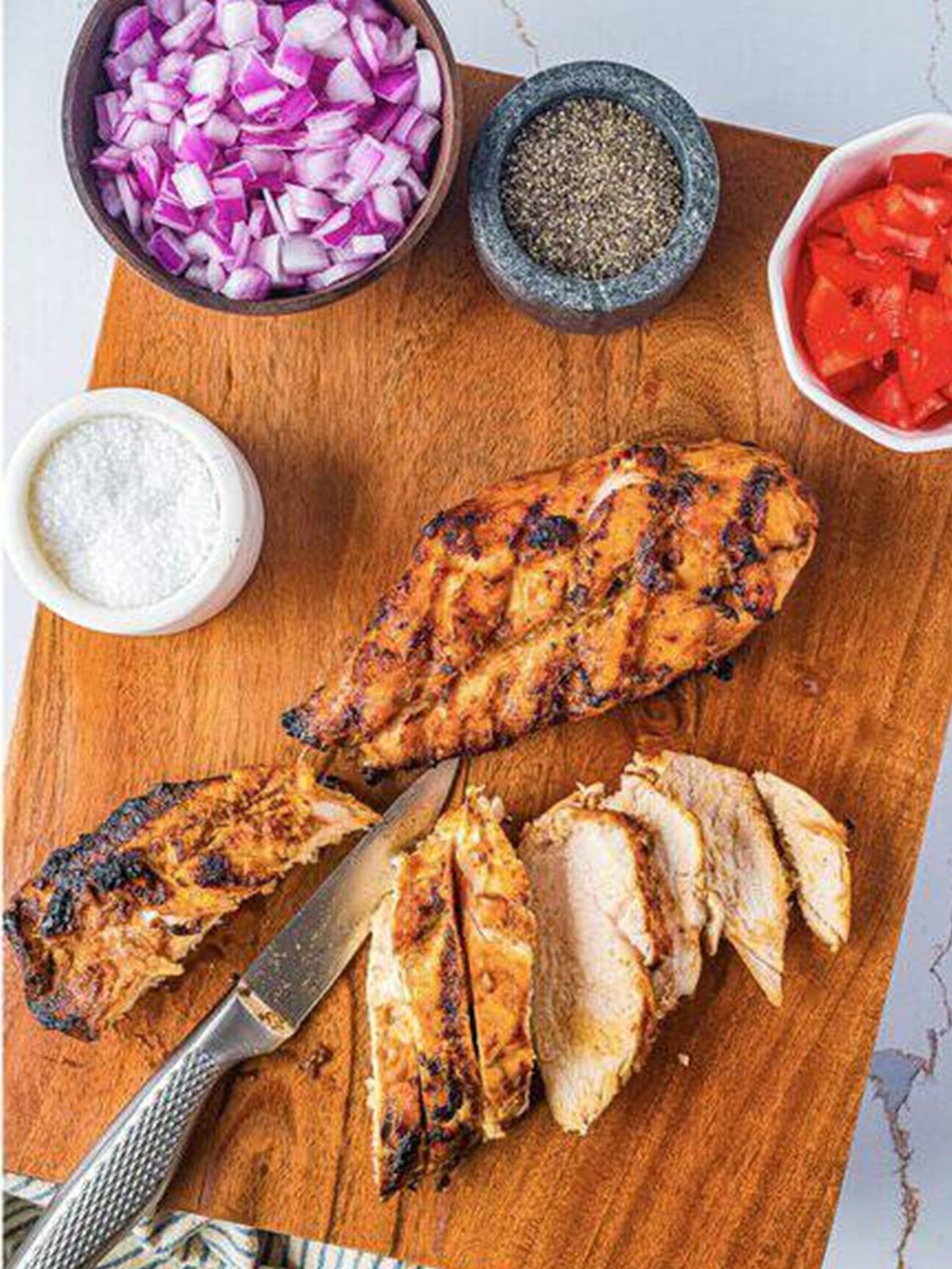 Sliced grilled chicken on a cutting board with taco toppings.