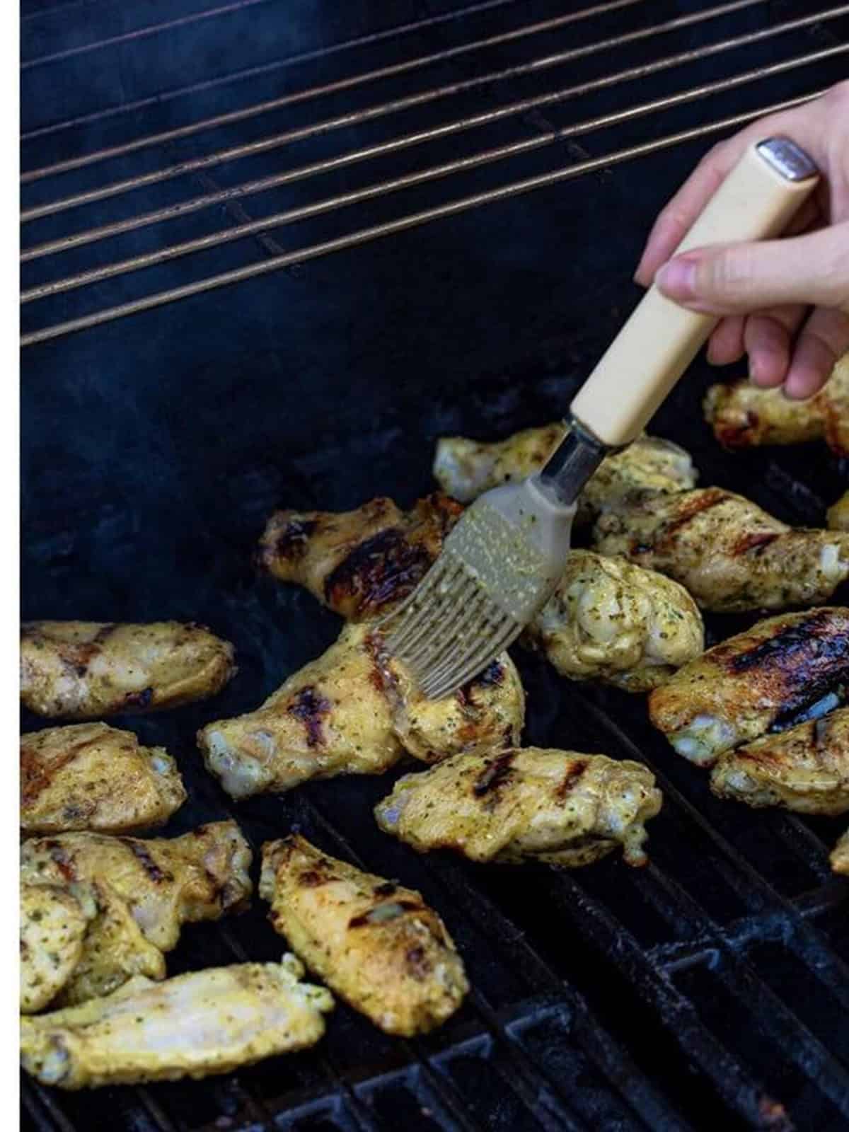 Basting Grilled Chicken Wings with marinade on the grill.