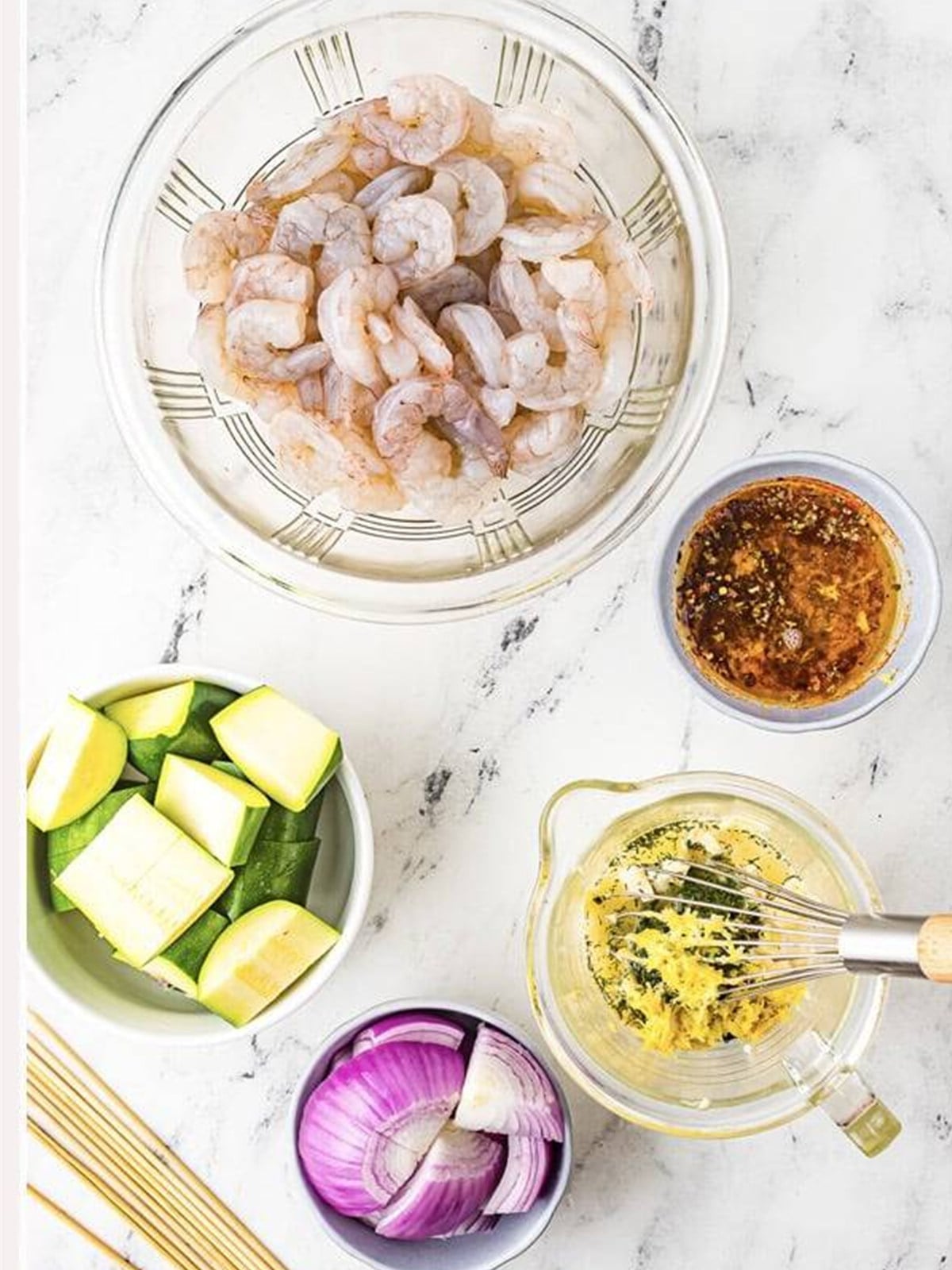 Shrimp, zucchini, and red onion with marinade for grilled shrimp skewers.