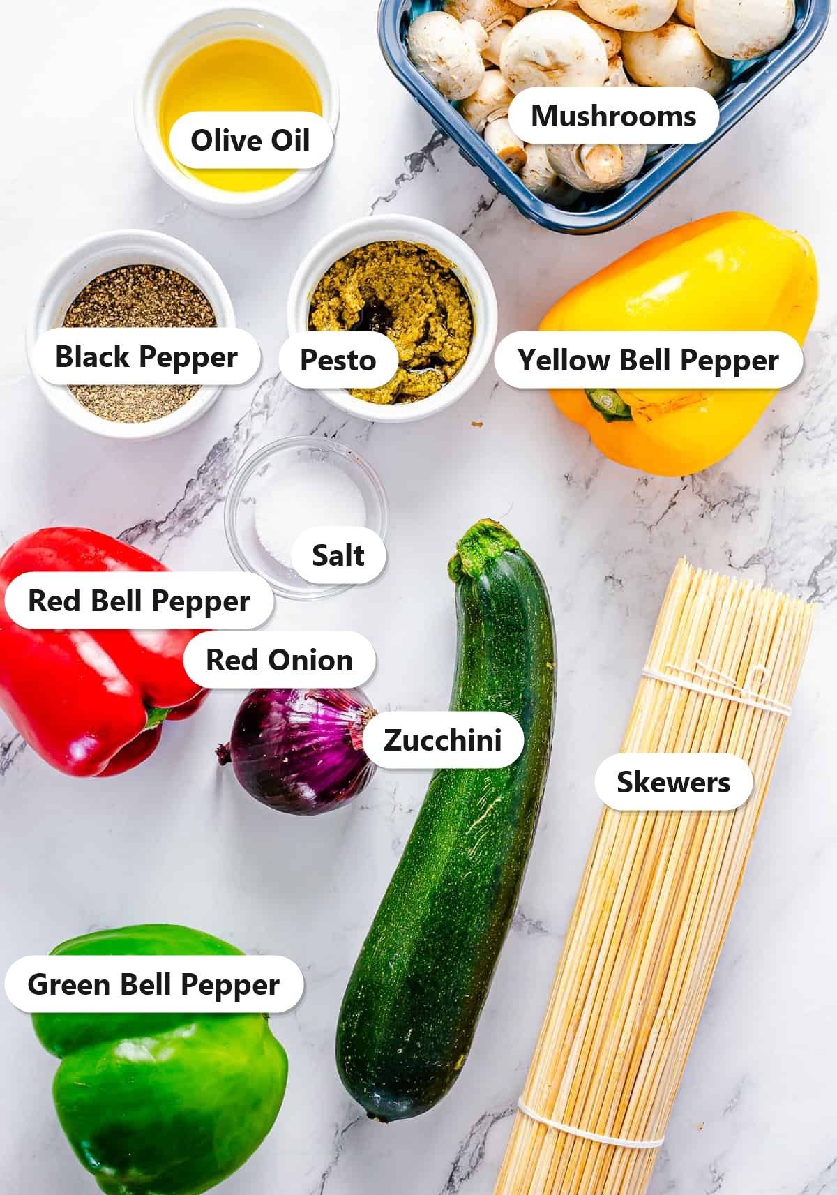 Labeled ingredients for grilled vegetable skewers including mushrooms, bell peppers, zucchini, red onion, pesto, and olive oil.