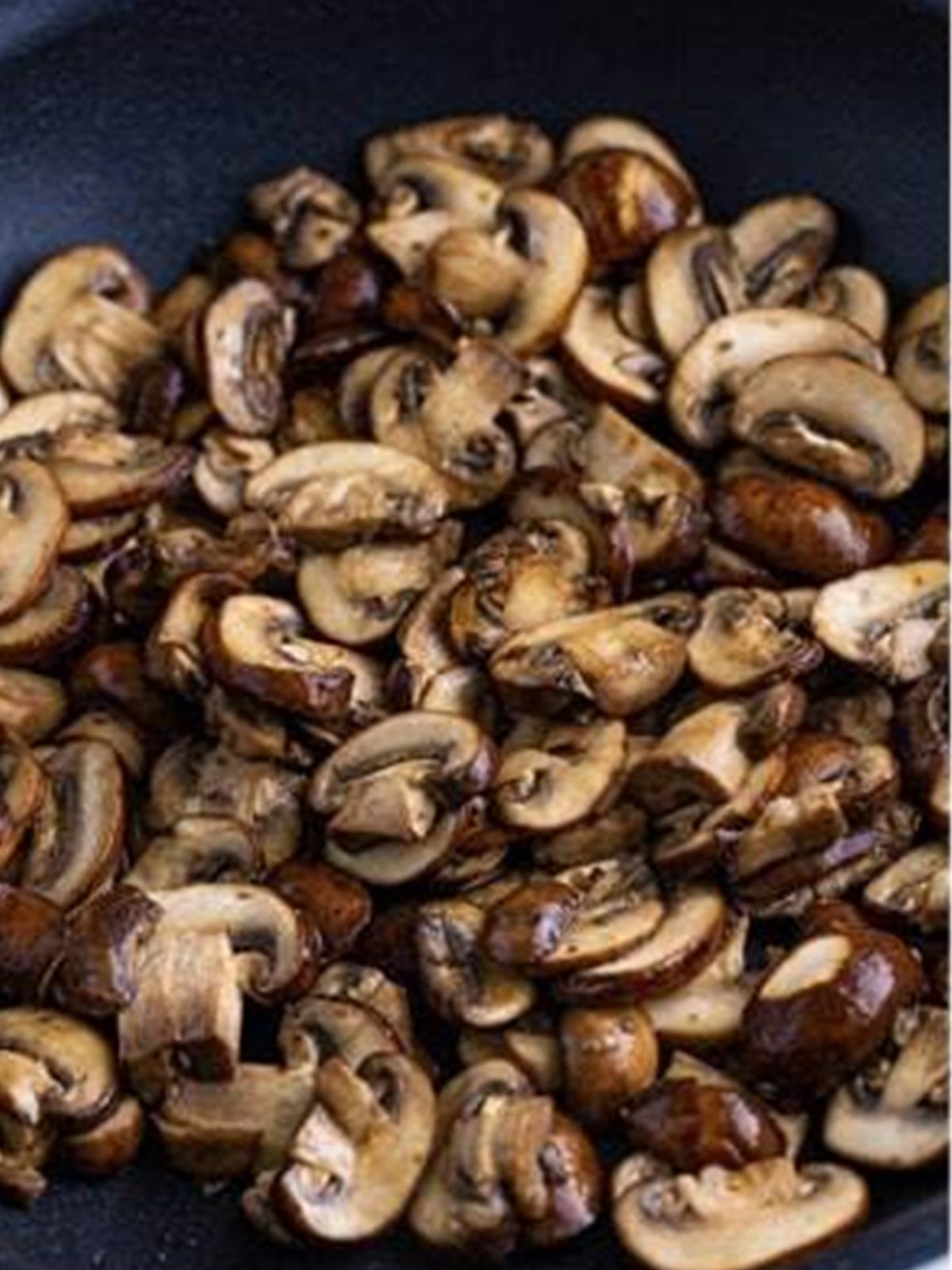 Sliced mushrooms searing in butter in a skillet for ground beef stroganoff.