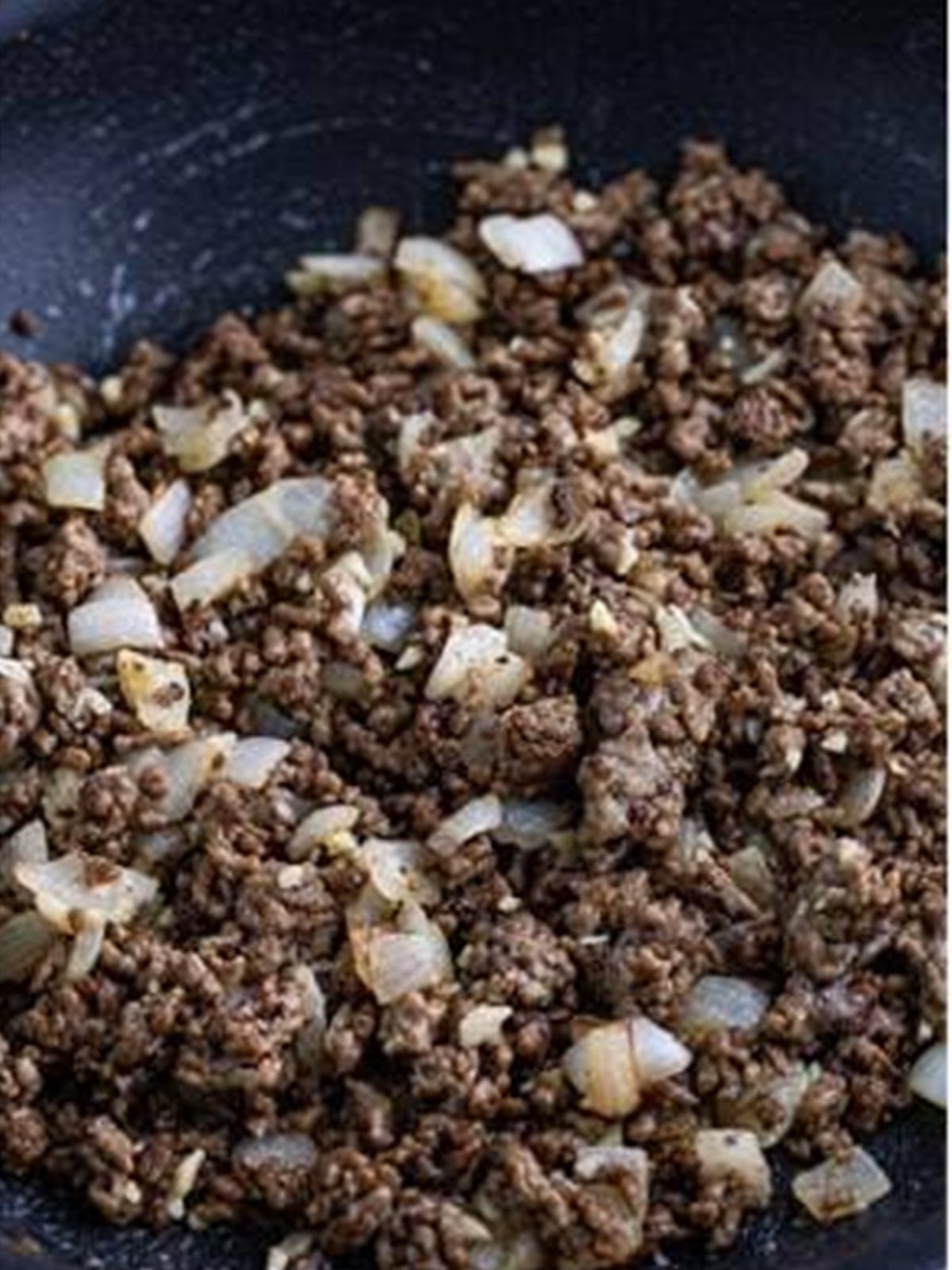 Onions and garlic added to the browned ground beef in a skillet.