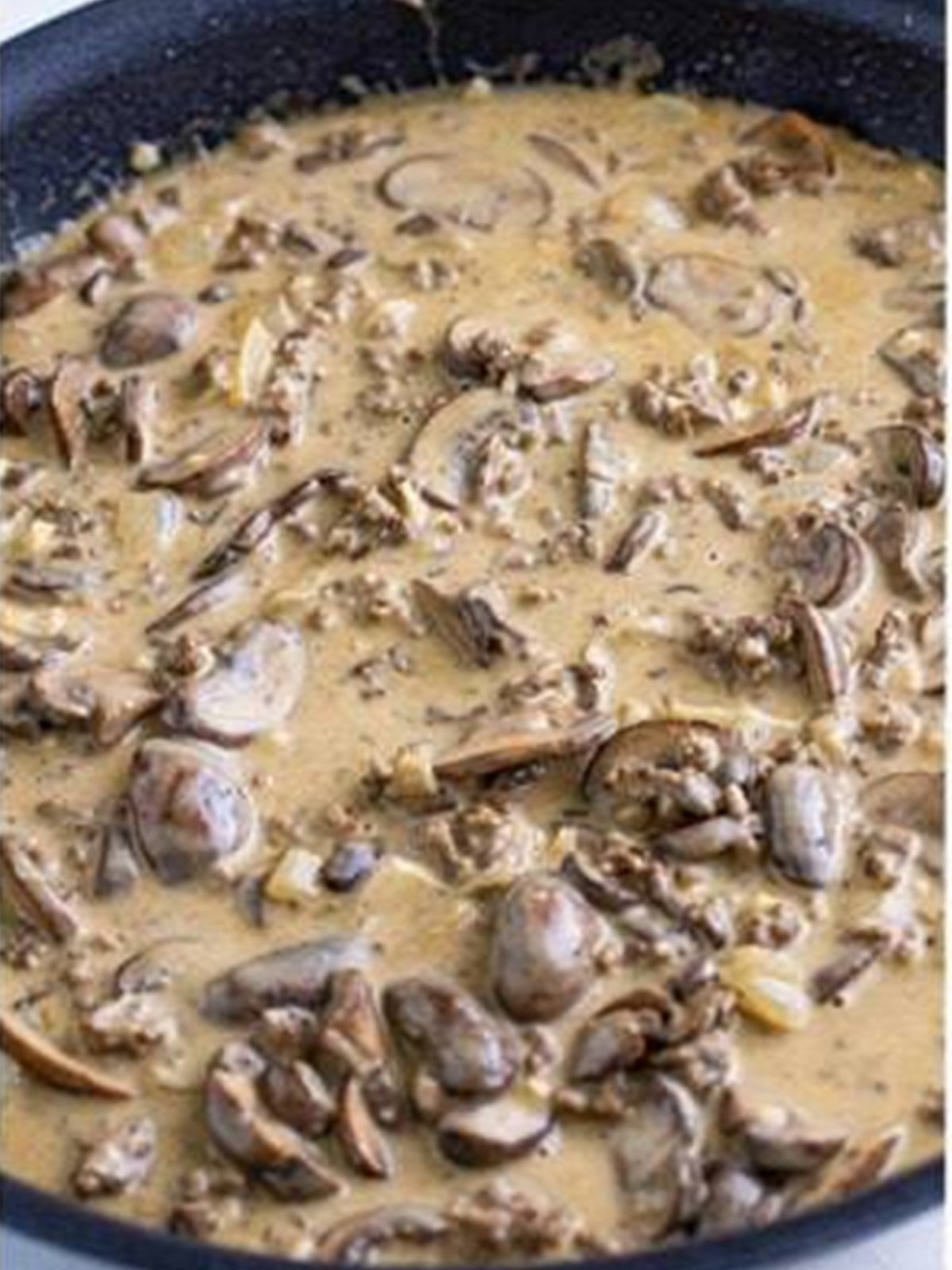 Ground beef stroganoff sauce simmering with mushrooms in a skillet.