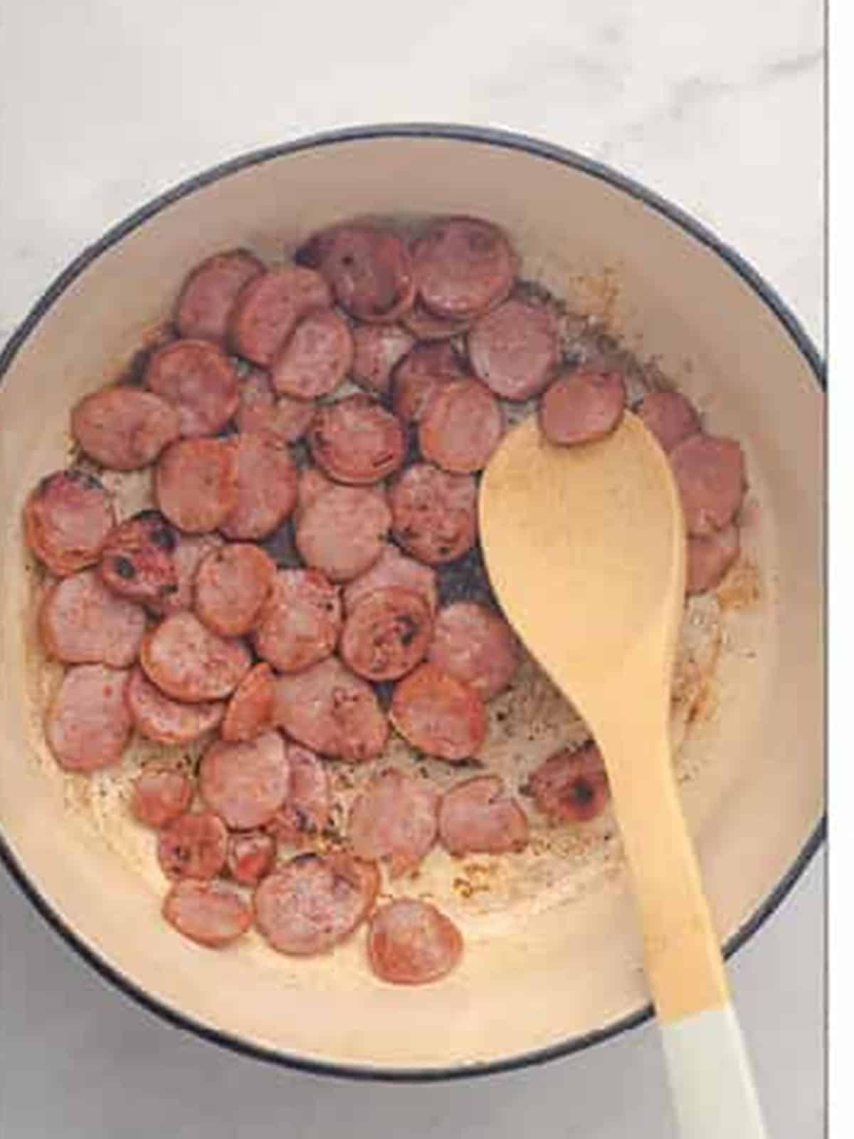 Andouille sausage slices browning in a heavy pot for gumbo.