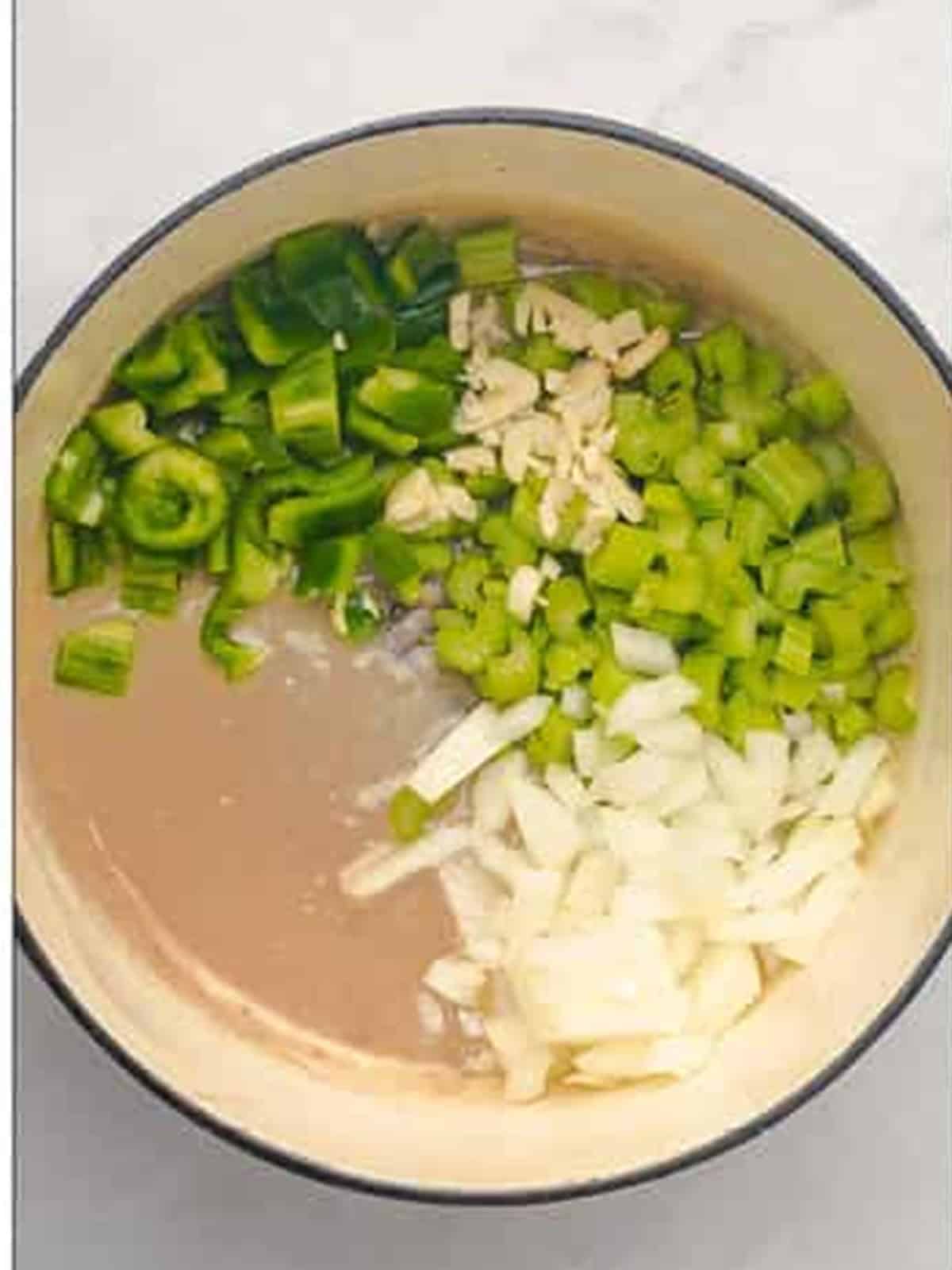 Adding chopped onion, bell pepper, celery, and garlic to the roux for gumbo.