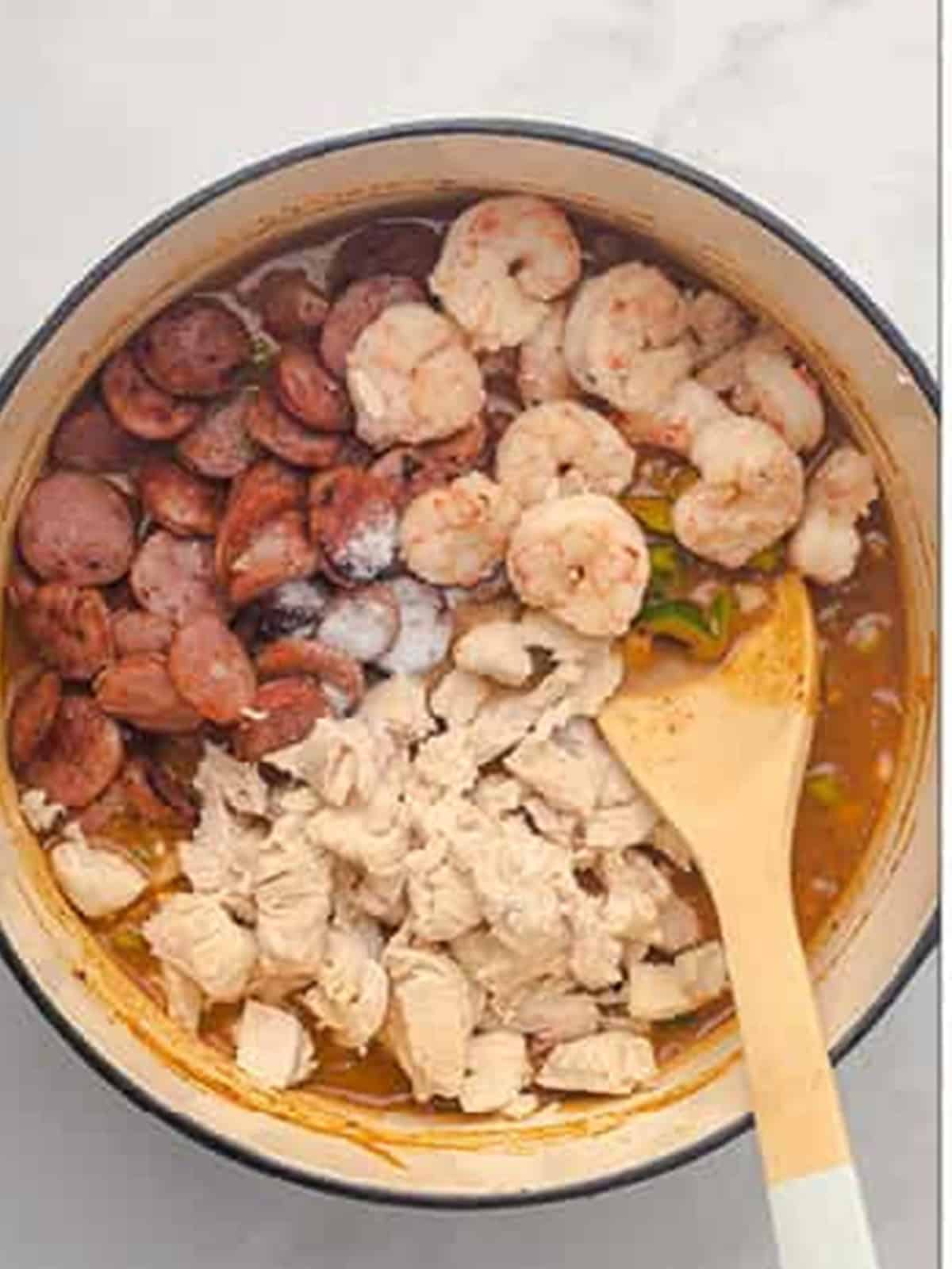 Adding browned sausage, chicken, and shrimp to the simmering gumbo.