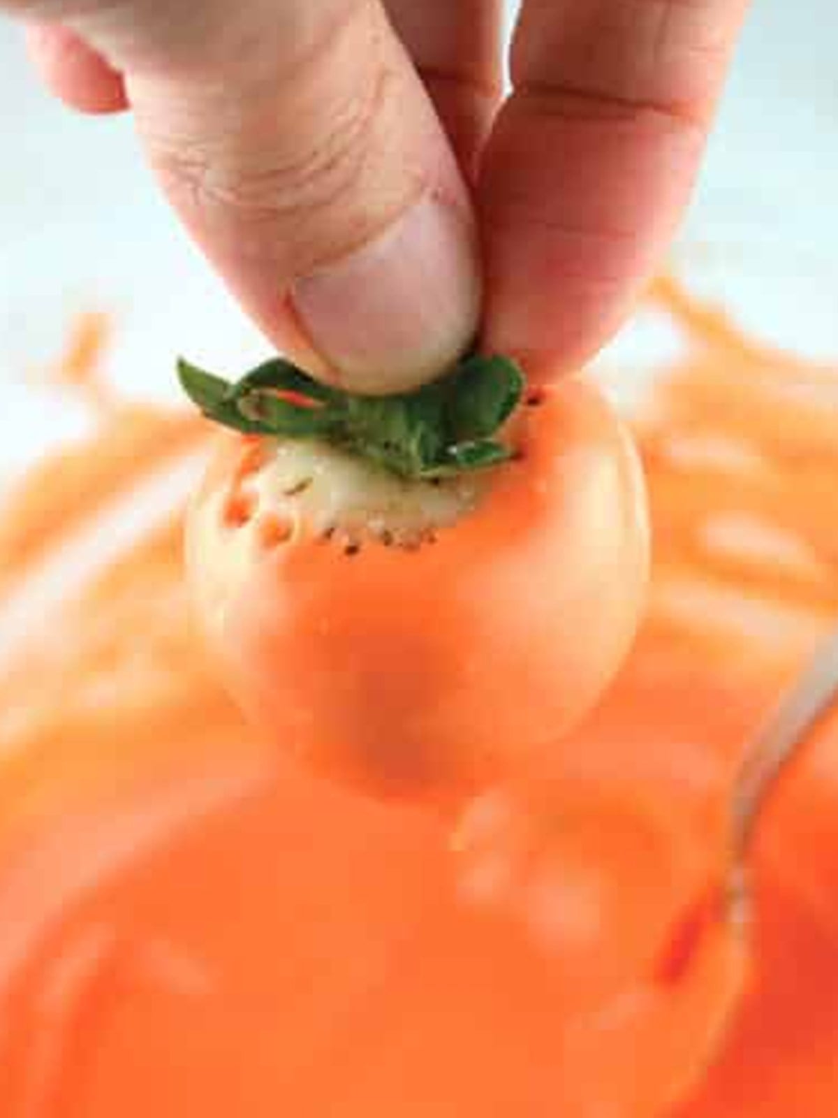 Dipping a strawberry into melted orange candy to make a halloween chocolate covered strawberry pumpkin.