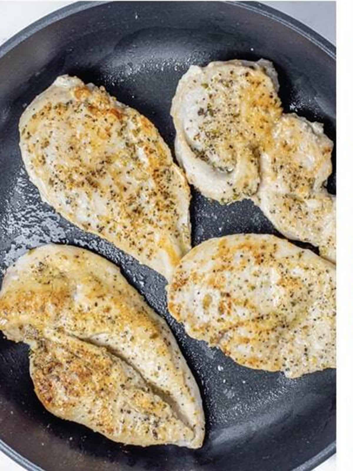 Seasoned chicken breasts searing in an oven-safe skillet.