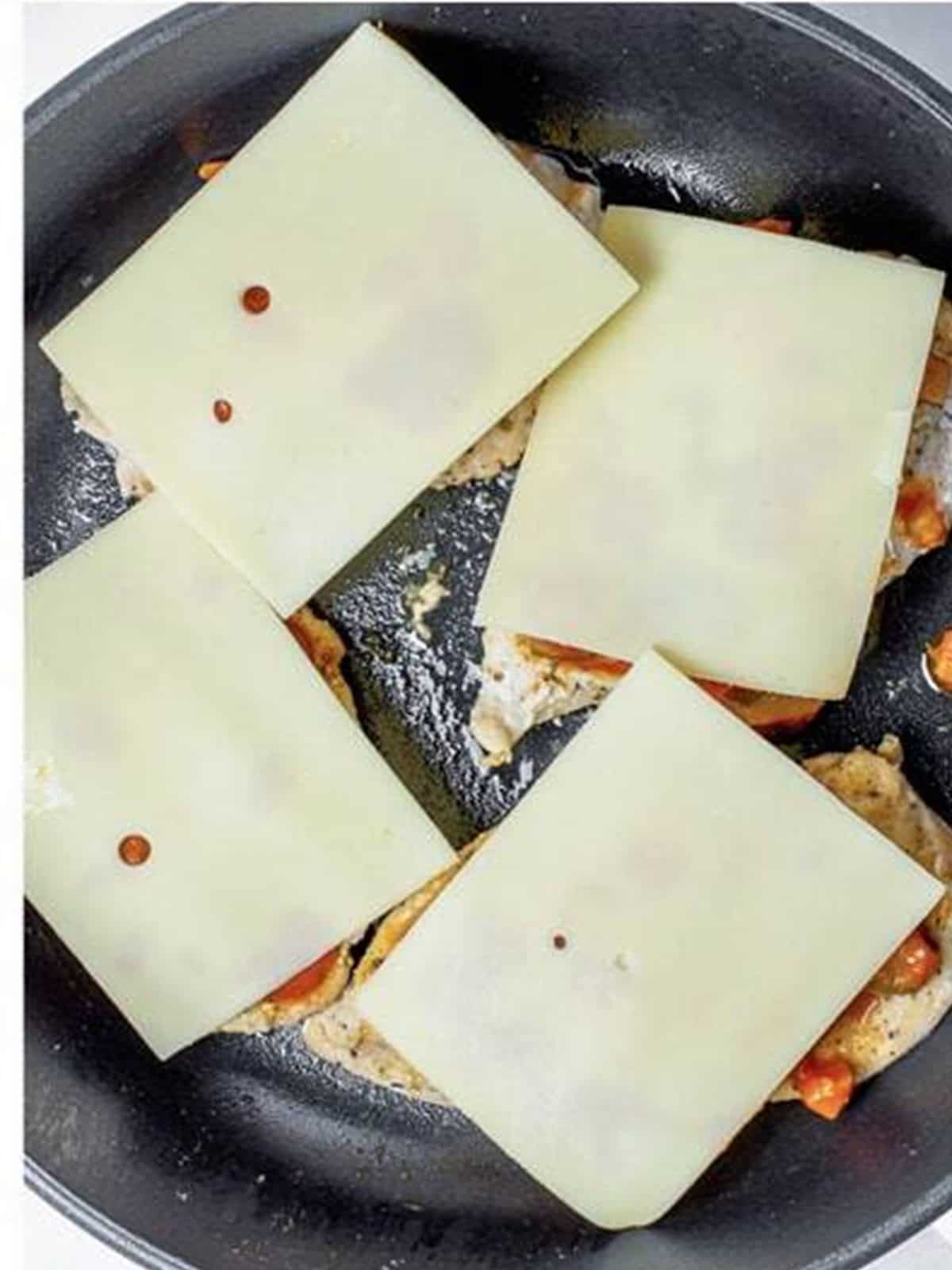 Provolone cheese slices added on top of the saucy chicken before baking.