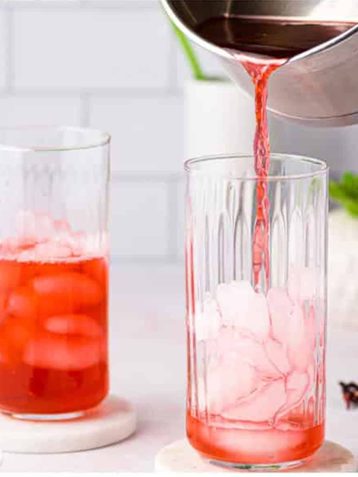 Red hibiscus tea being poured over ice in a tall glass.