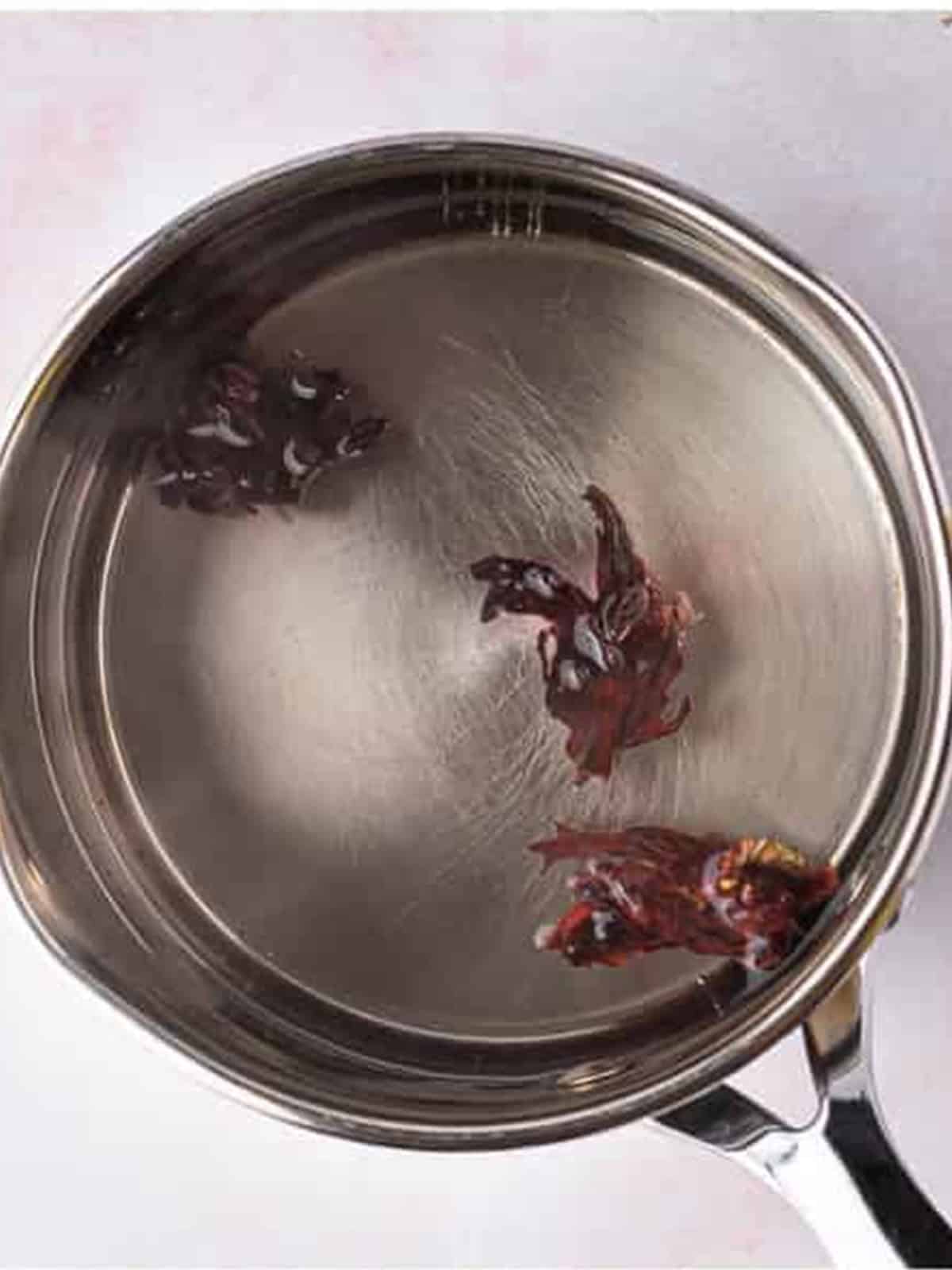 Dried hibiscus flowers steeping in hot water in a saucepan to make hibiscus tea.