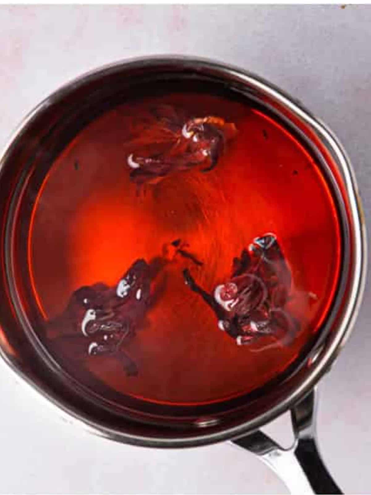 Deep red steeped hibiscus tea in a saucepan ready to cool.