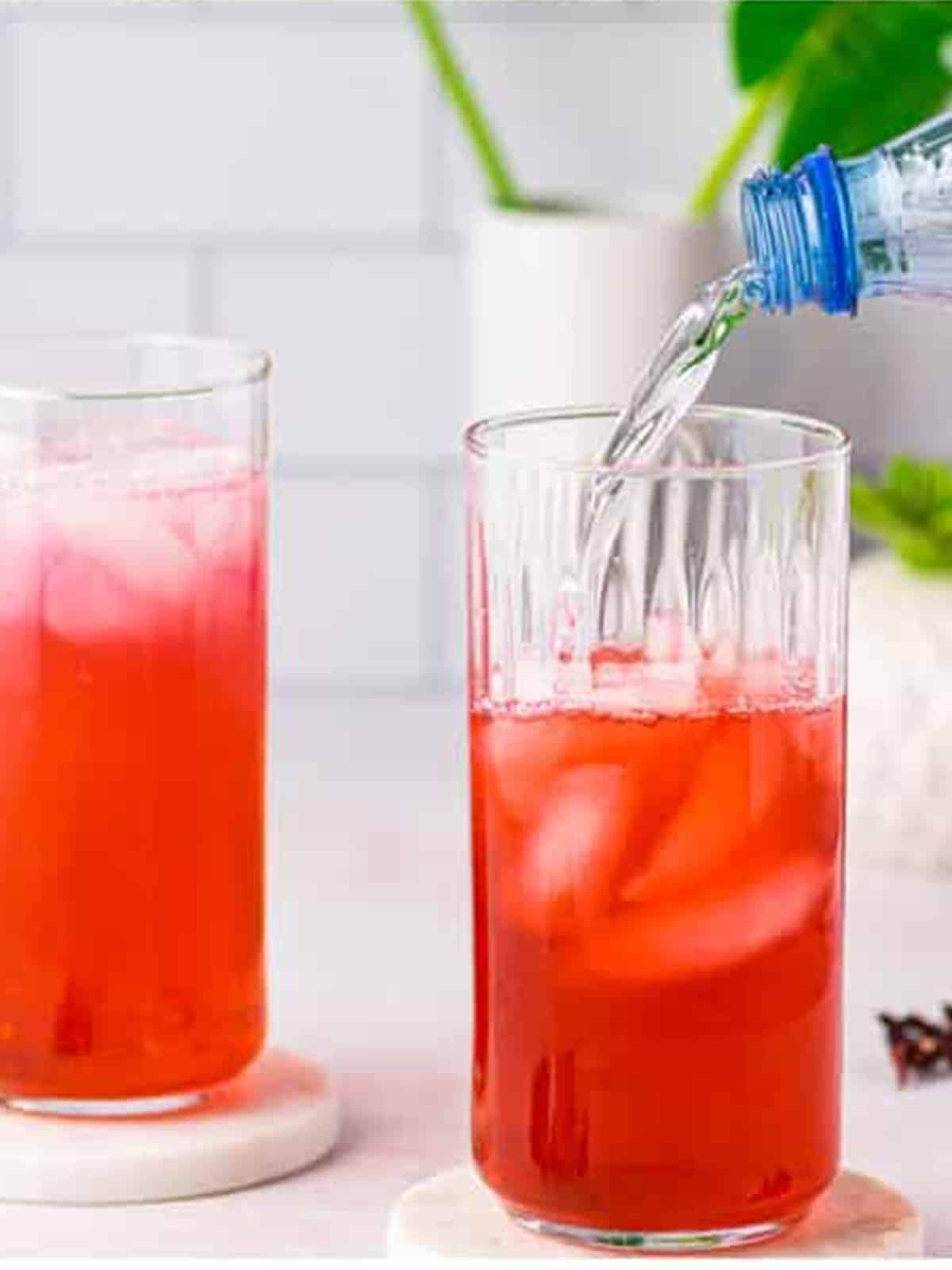 Sparkling water being added to a glass of iced hibiscus tea.