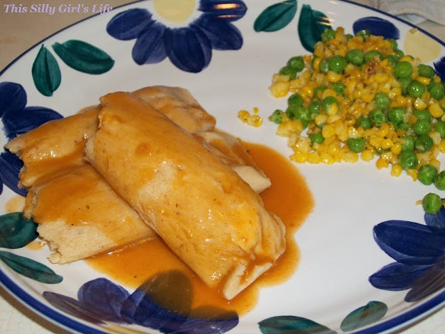A plate of homemade chicken tamales topped with red sauce.